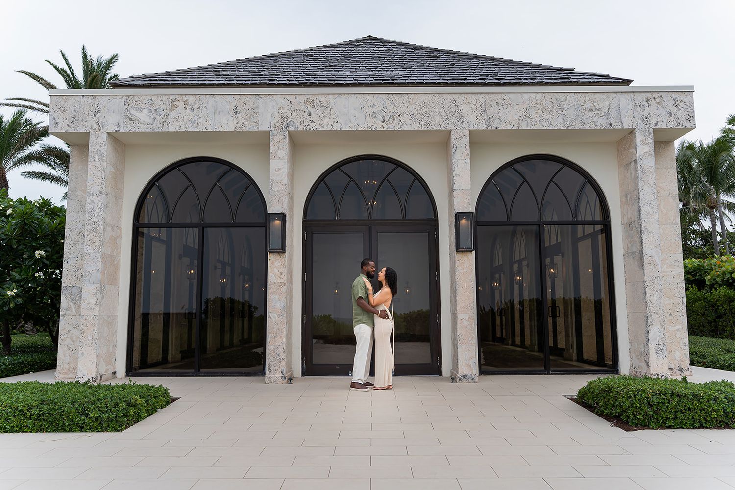 Couple embracing in front of elegant arched stone building with black doors at a luxury resort.