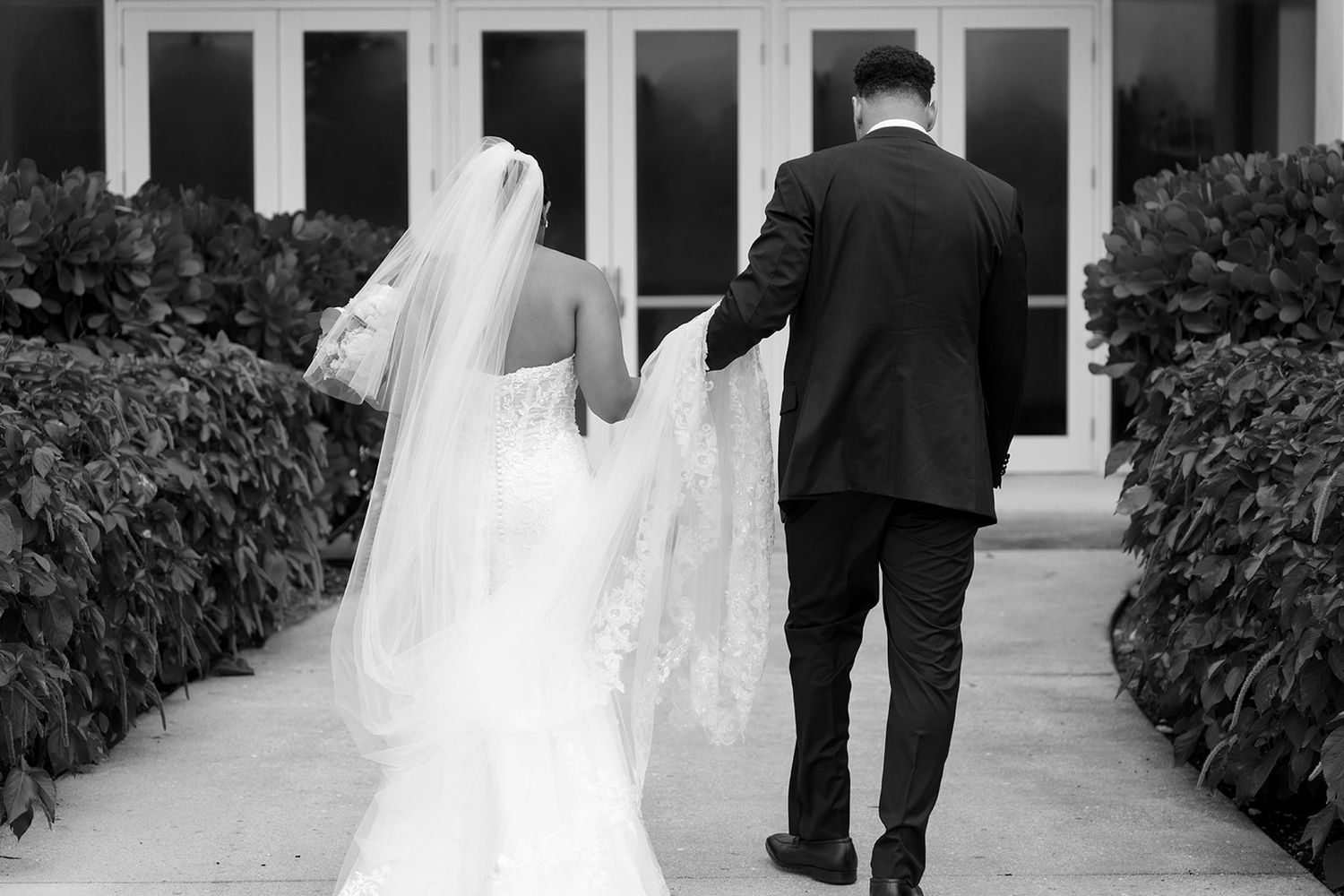 Bride and groom walking hand in hand in black and white wedding photo.