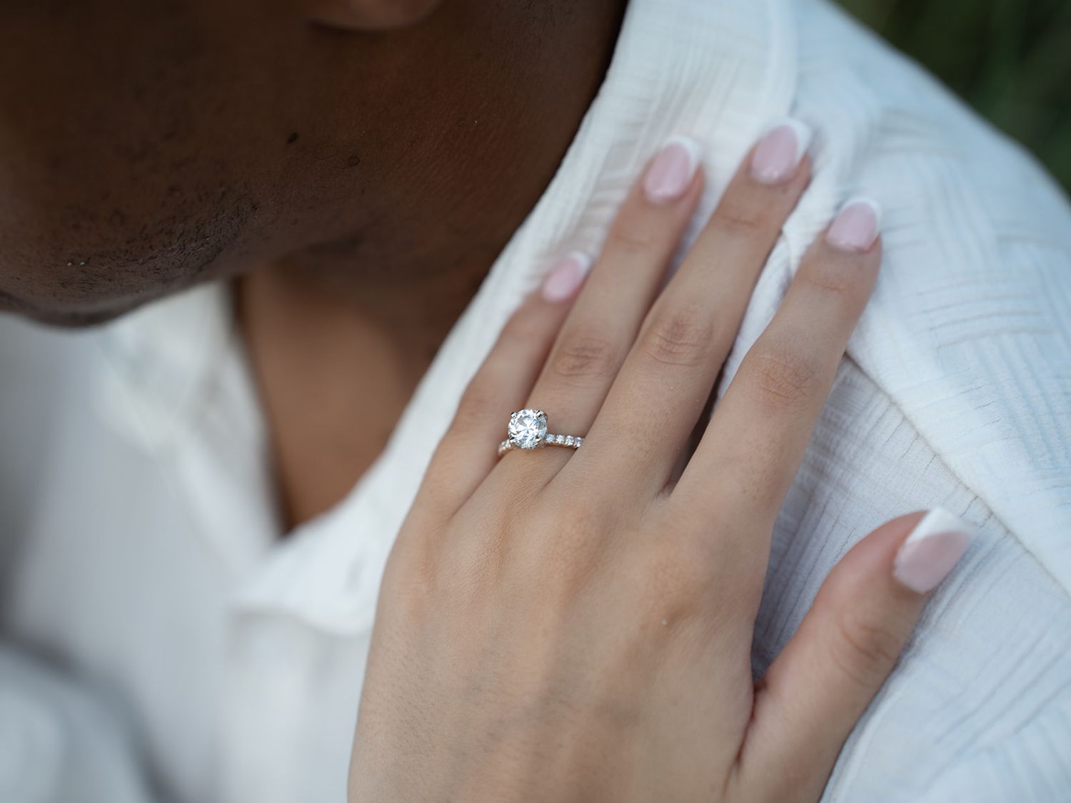 Close-up of a diamond solitaire engagement ring on a woman's hand resting on a white shirt.