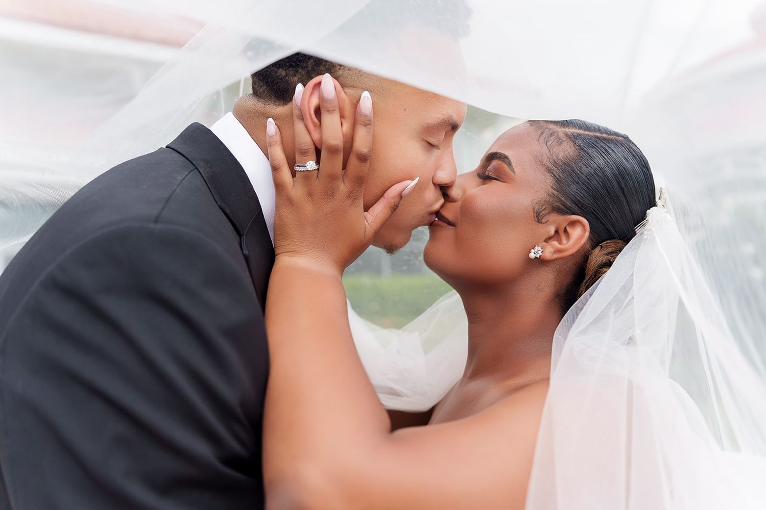 Bride and groom sharing a romantic kiss under a wedding veil on their special day.
