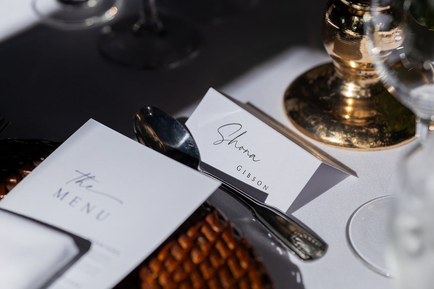 Elegant wedding place setting with a menu card, silverware, and a name card reading Shona on a wicker placemat.