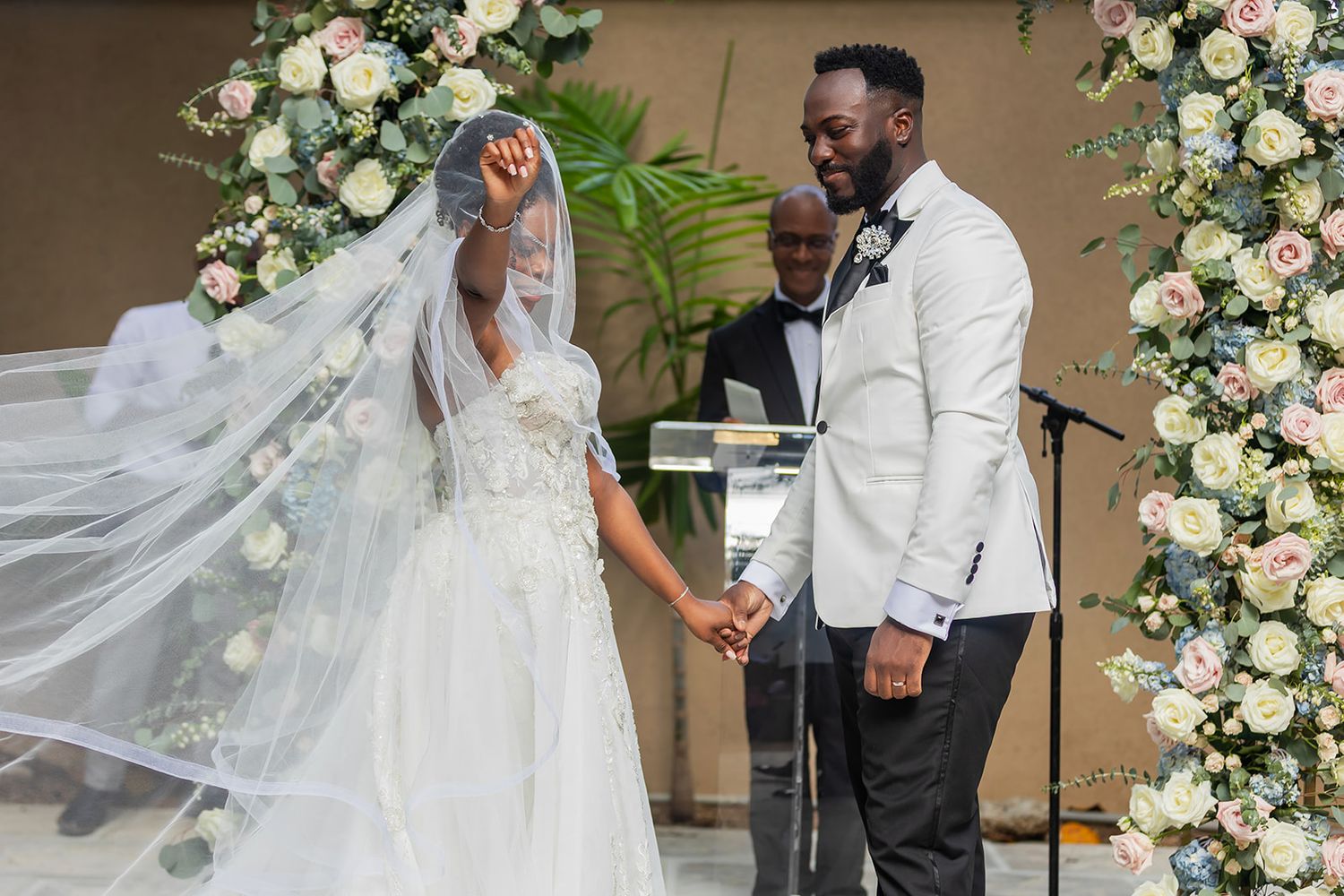 Bride and groom exchange vows at elegant wedding ceremony with floral arch backdrop.