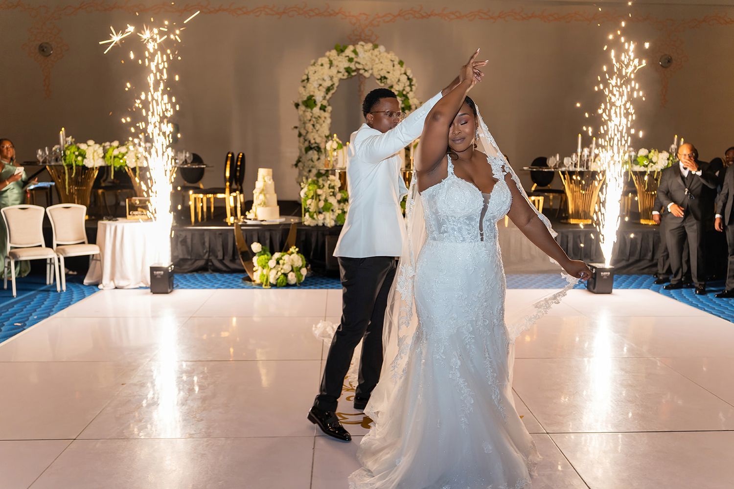 Bride and groom share first dance on white floor with sparkling fountains at elegant wedding reception.