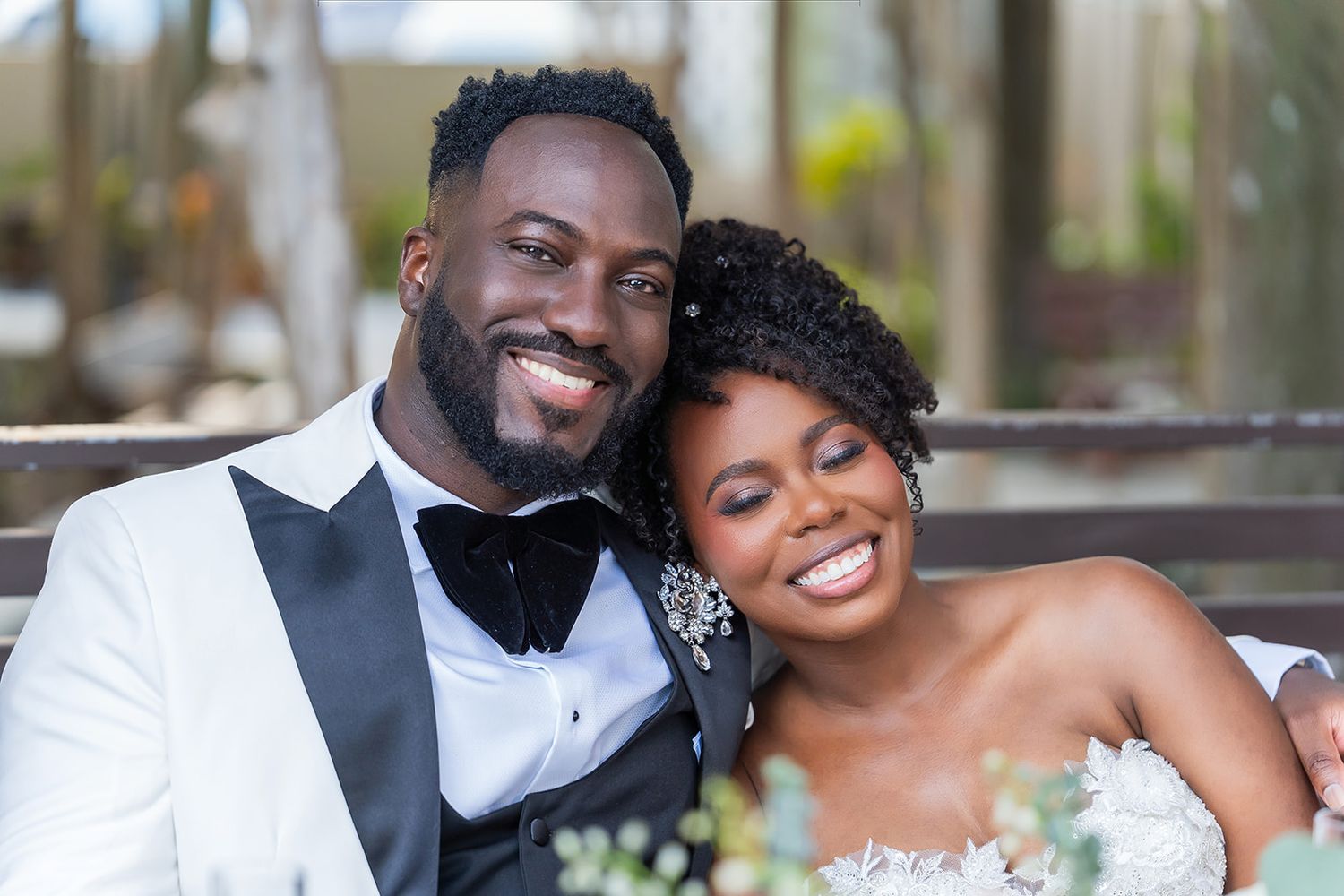 Happy newlywed couple smiling together, groom in white tuxedo and bride in strapless wedding gown.