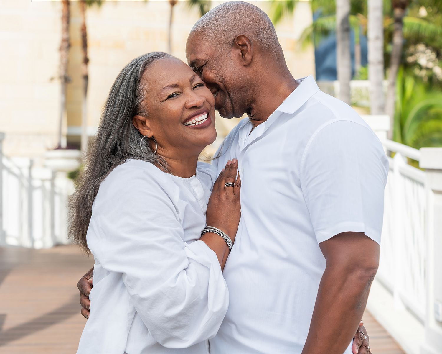 Happy older Black couple in white outfits sharing a romantic moment outdoors, smiling and embracing affectionately.