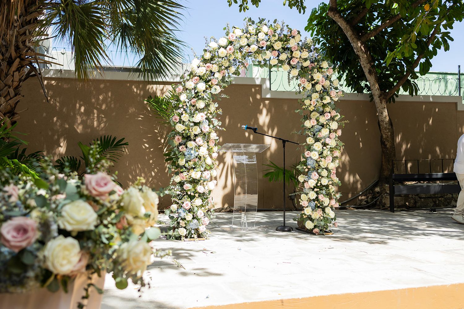 Elegant outdoor wedding ceremony arch adorned with white and pink flowers against a warm beige wall.