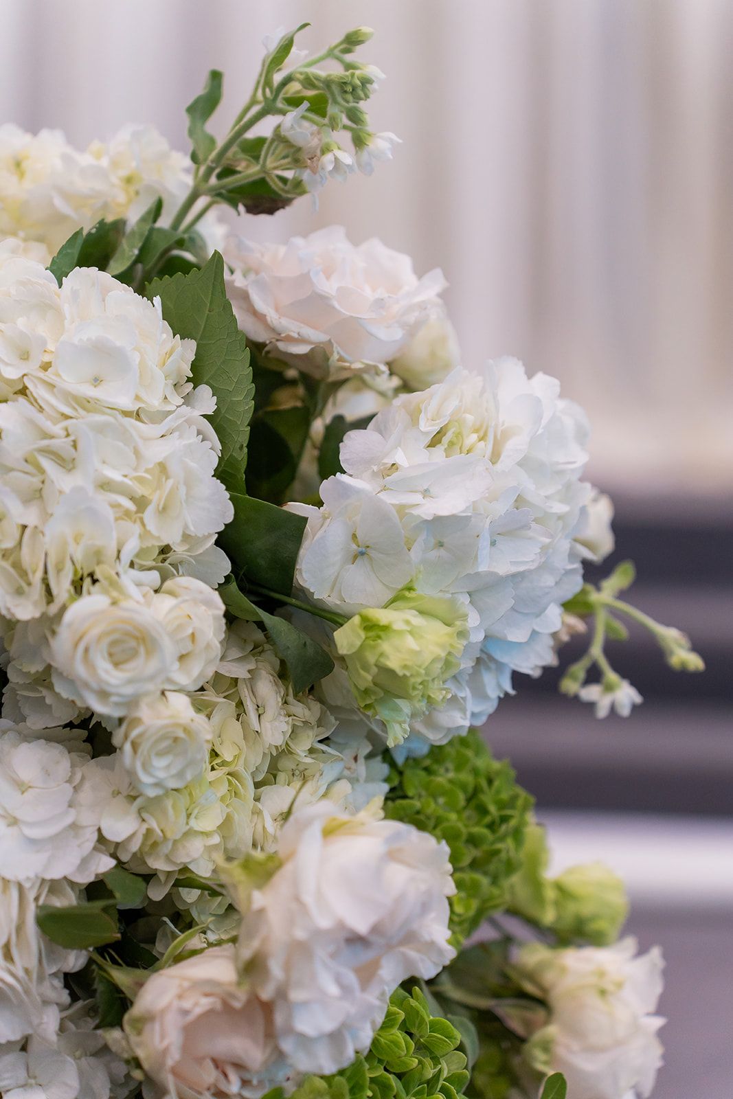 Elegant white hydrangea and rose floral arrangement with soft blue accents and green foliage for a wedding.