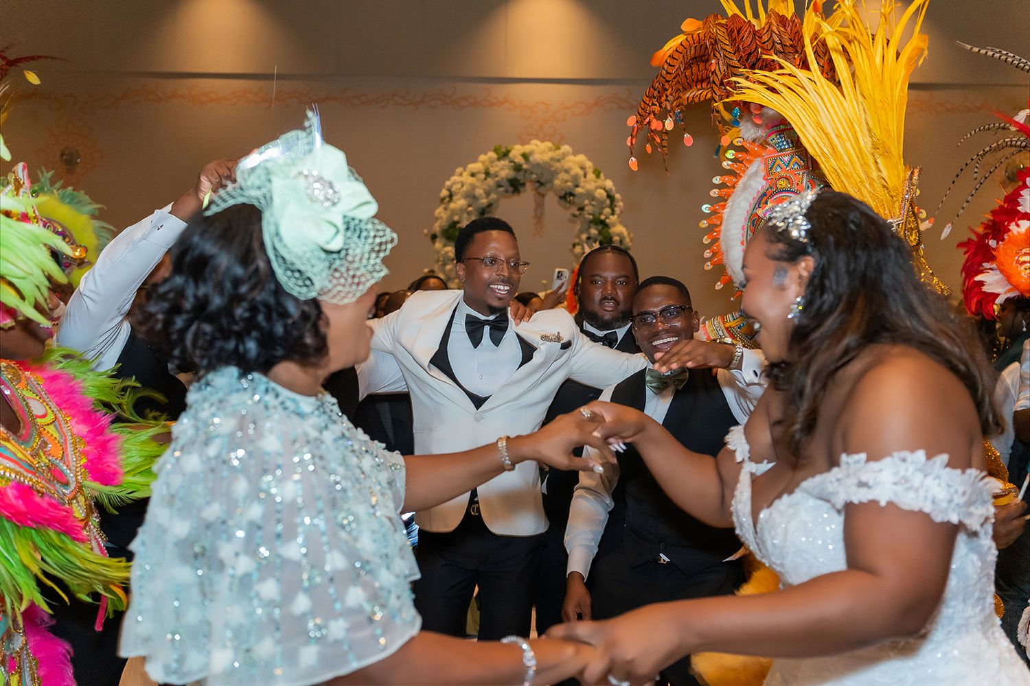 Bride and groom celebrate with guests in colorful carnival attire at a vibrant wedding reception dance.