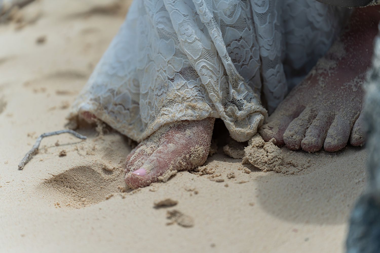 Close-up of sandy bare feet beneath a flowing gray dress on a beach.