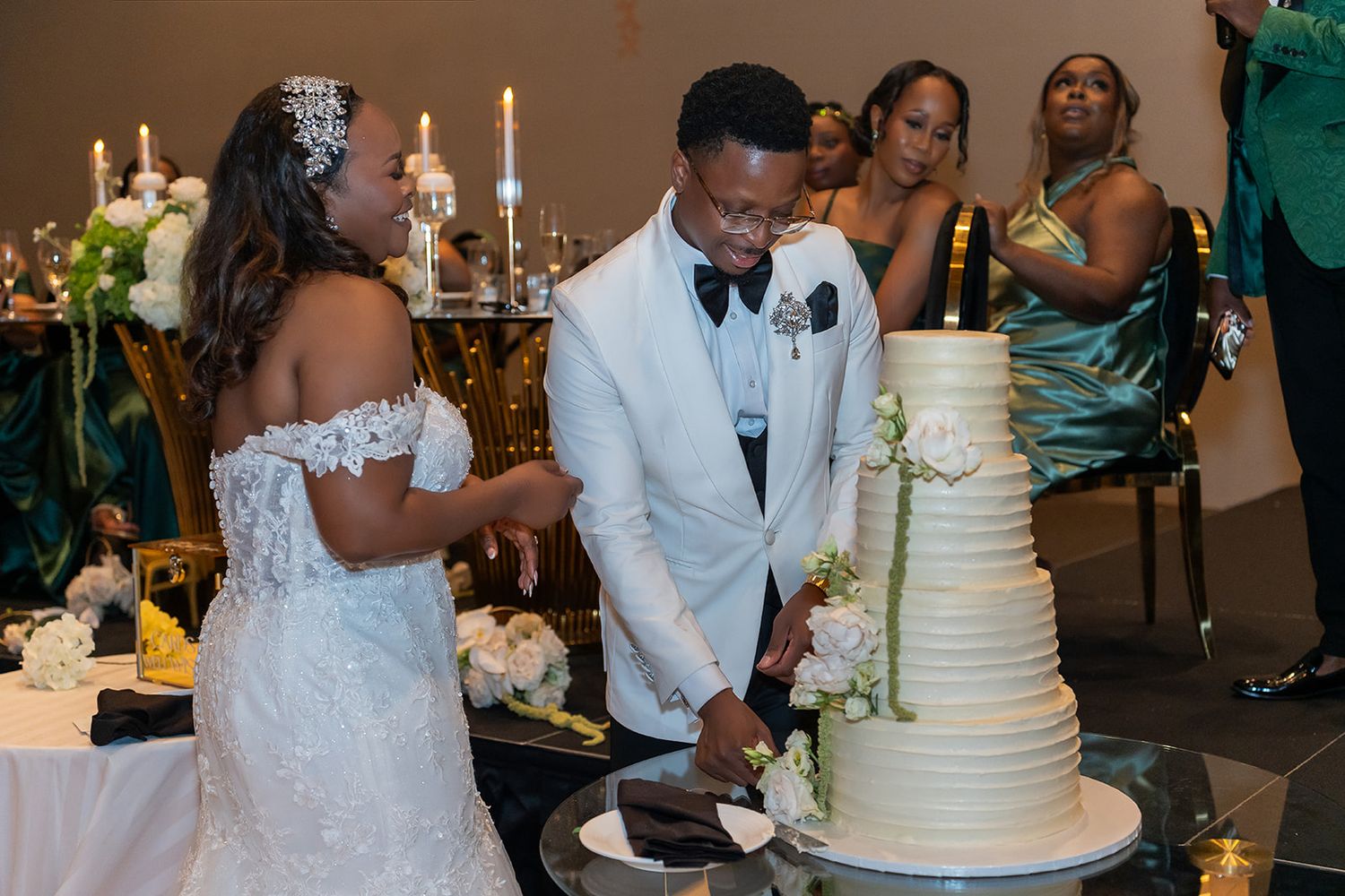 Bride and groom cut tiered white wedding cake together at elegant candlelit reception.