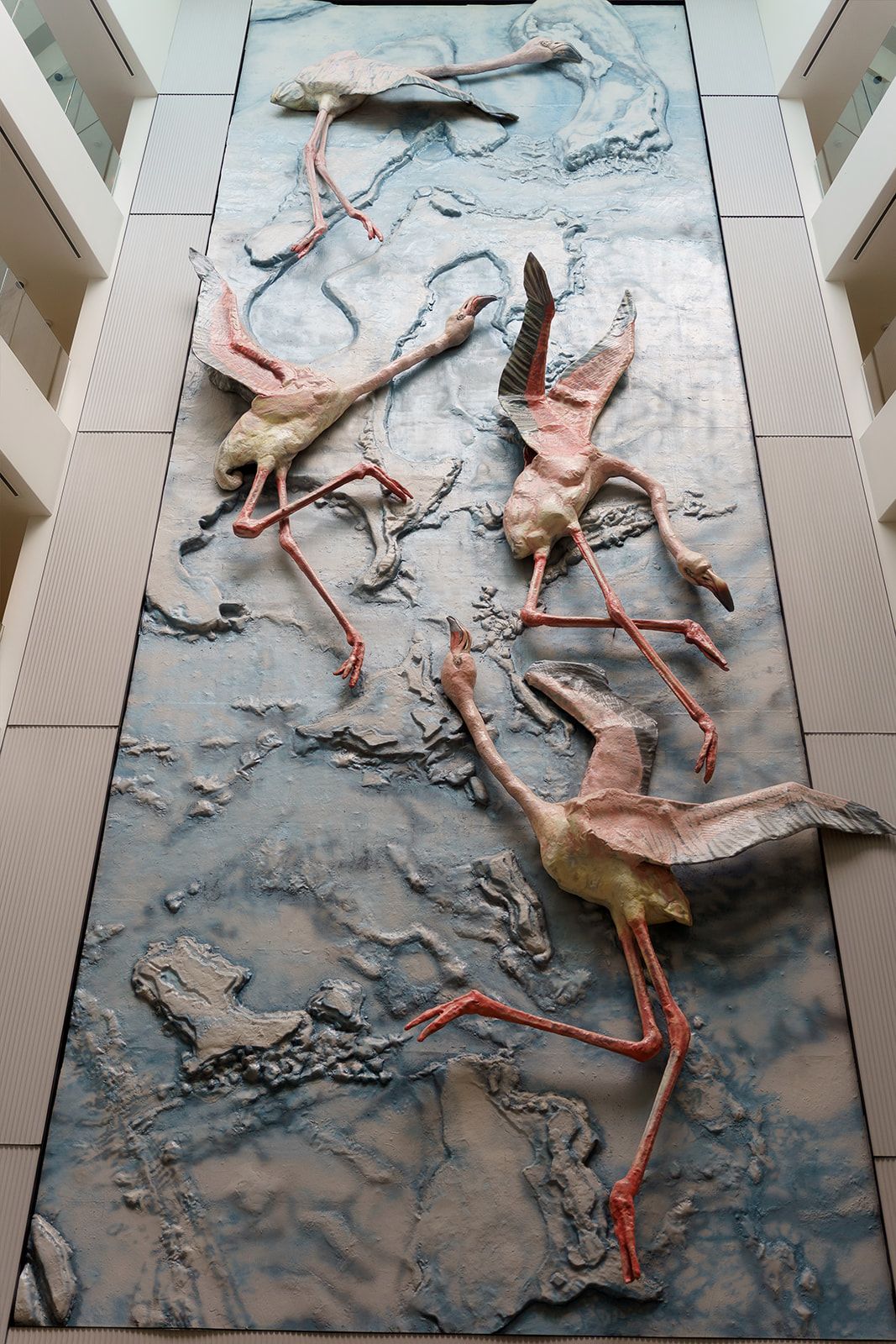 Large decorative wall relief sculpture featuring flamingos in flight, displayed in a modern building interior.