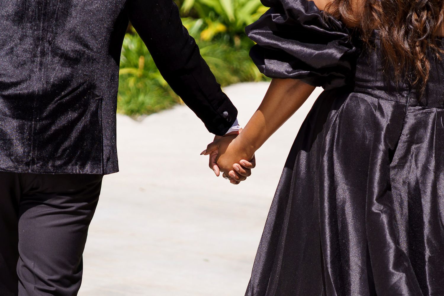 Close-up of couple holding hands in black formal attire while walking outdoors.