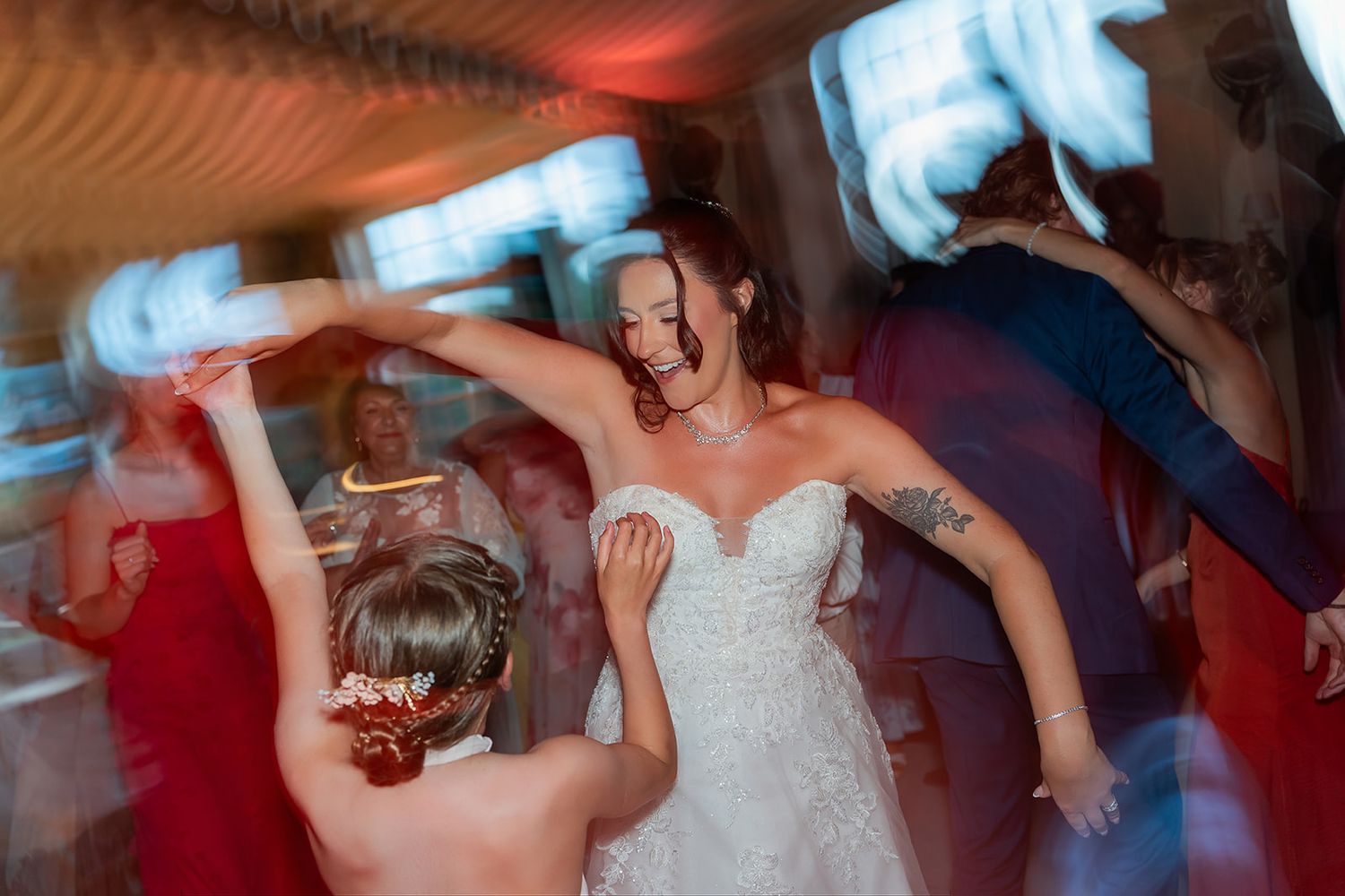Bride in lace wedding dress dancing joyfully with guests at a lively wedding reception party.