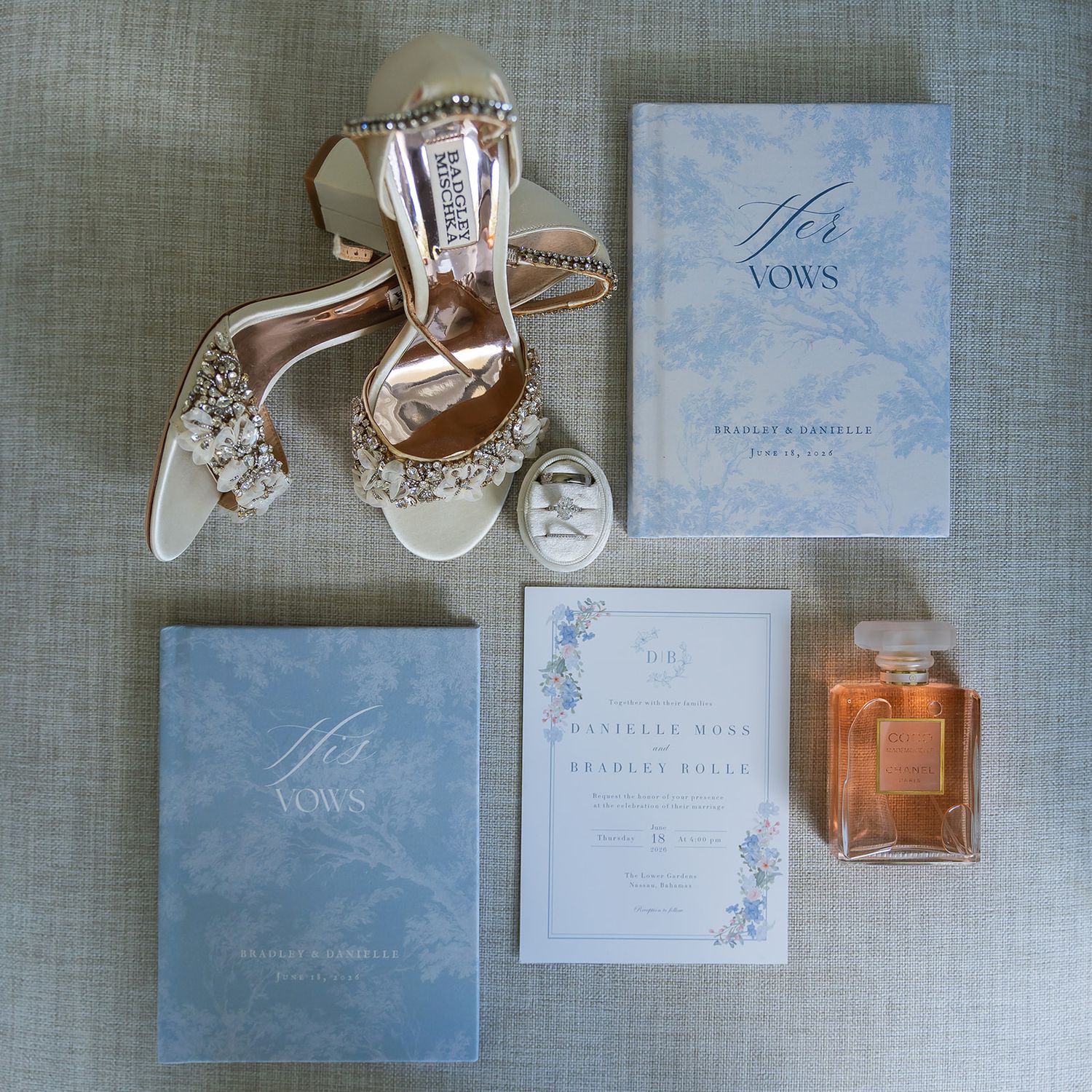Elegant wedding flat lay featuring Badgley Mischka bridal heels, vow books, floral invitation suite, and Chanel perfume.
