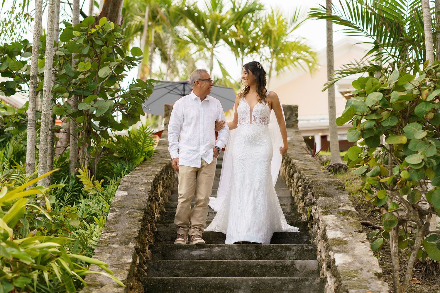 Bride and groom walking down stone steps surrounded by tropical greenery.