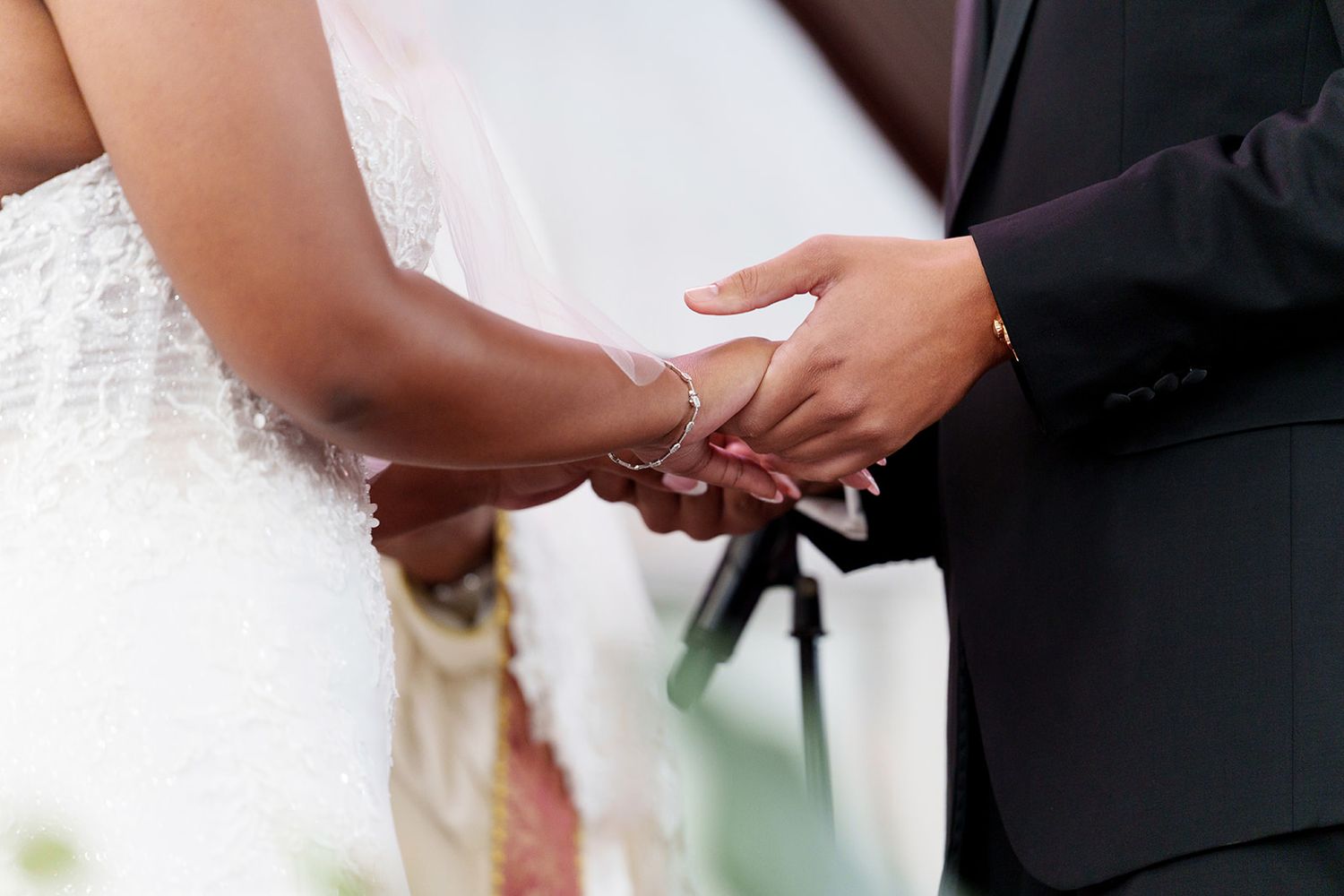 Bride and groom exchanging rings during wedding ceremony, close-up of hands holding together in elegant attire.