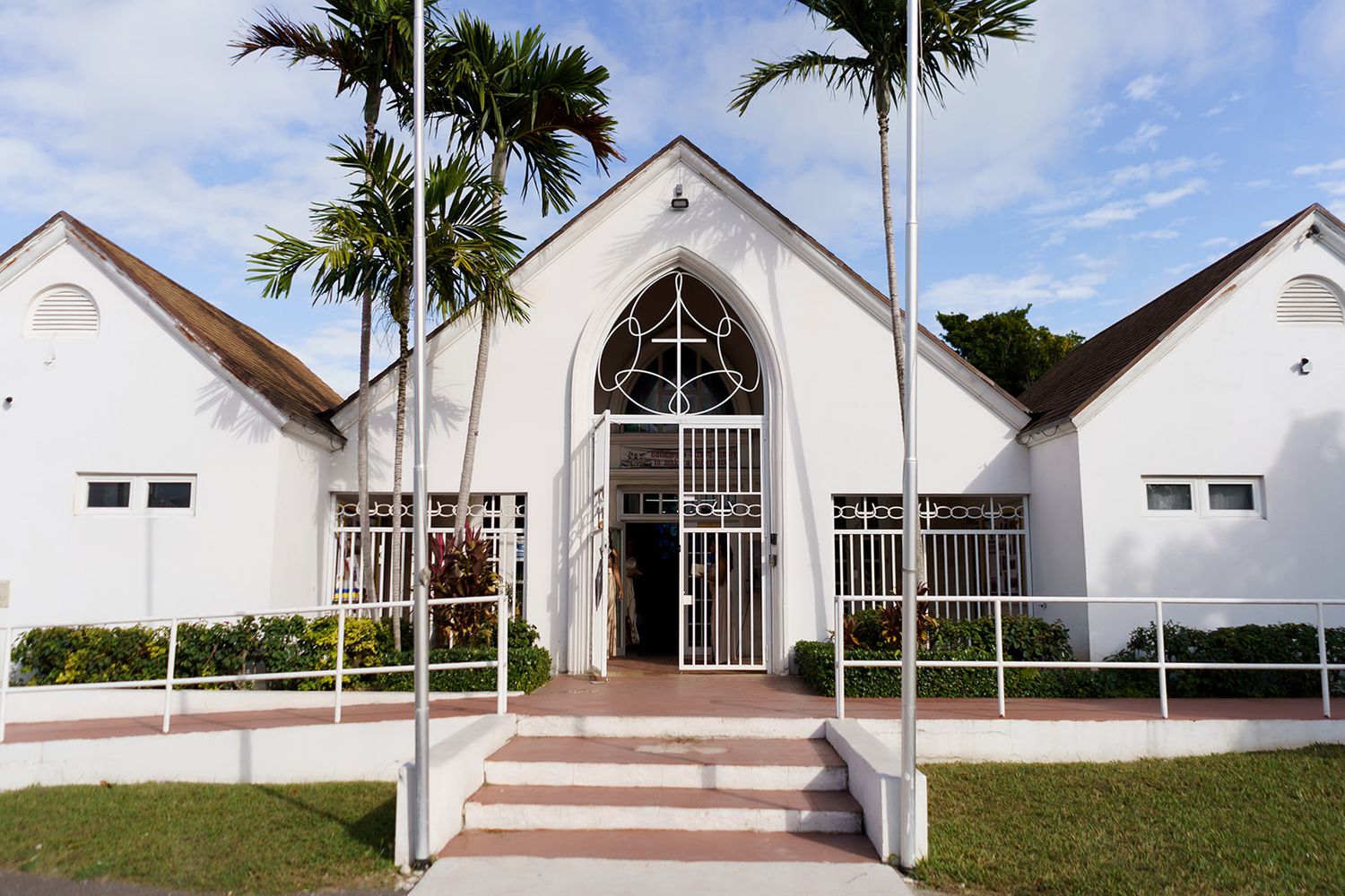 White church with arched gothic entrance, palm trees, and pink steps in a tropical setting.