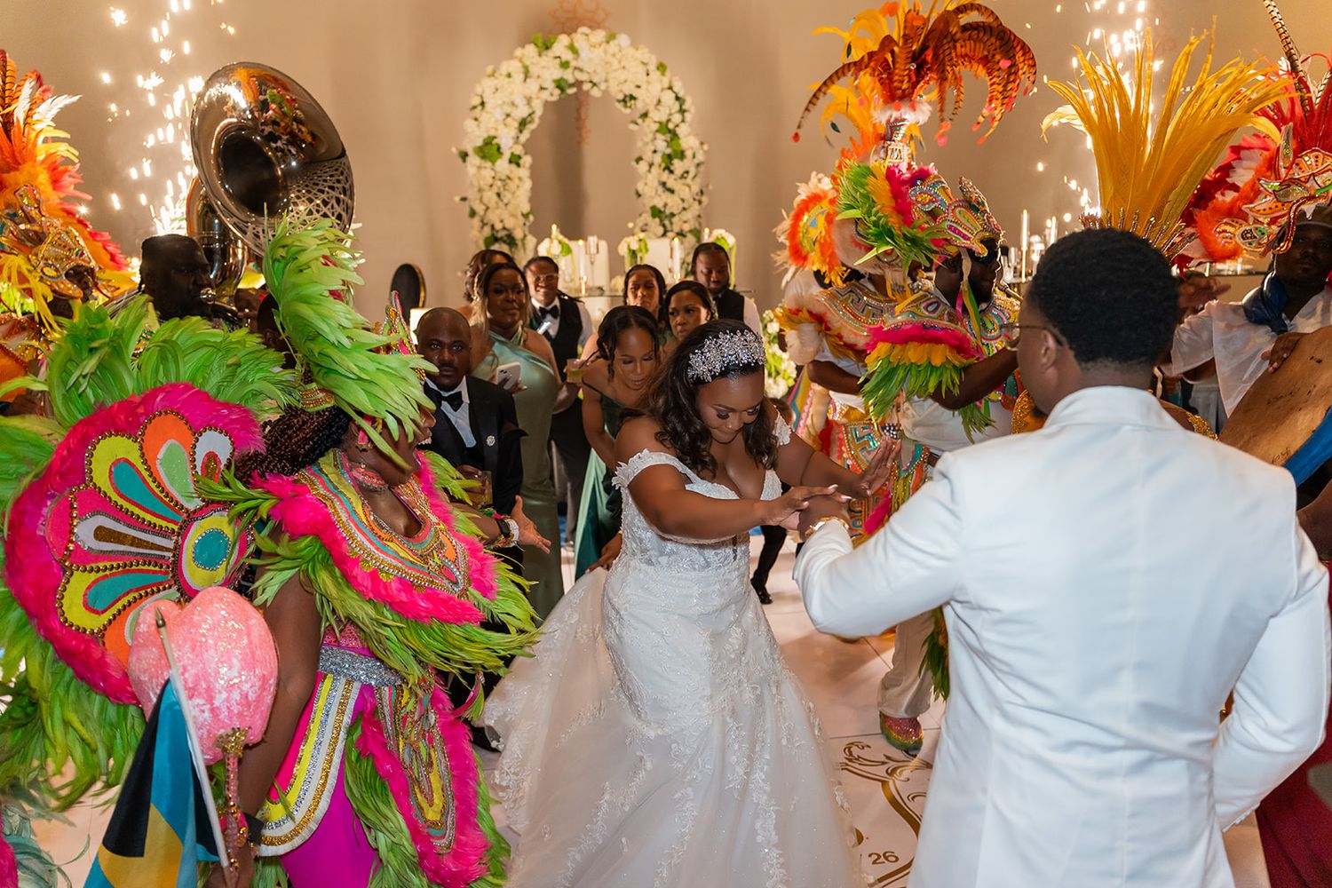 Bride and groom dance with colorful Mardi Gras performers at vibrant wedding reception celebration.