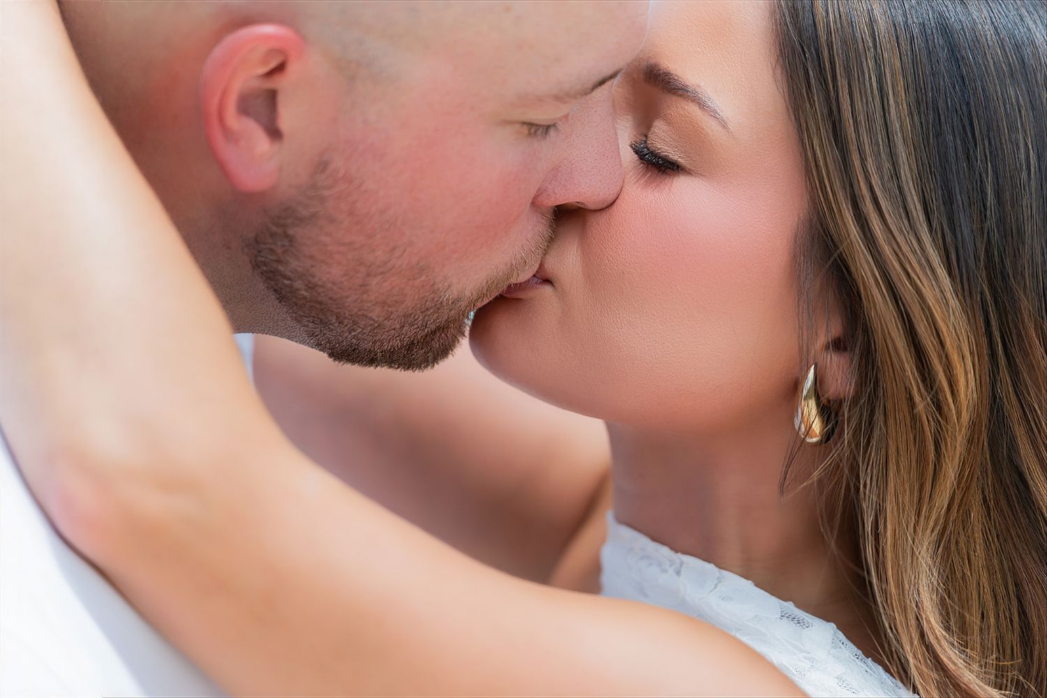Close-up of a couple sharing a romantic kiss, with the woman wearing a gold earring and white dress.