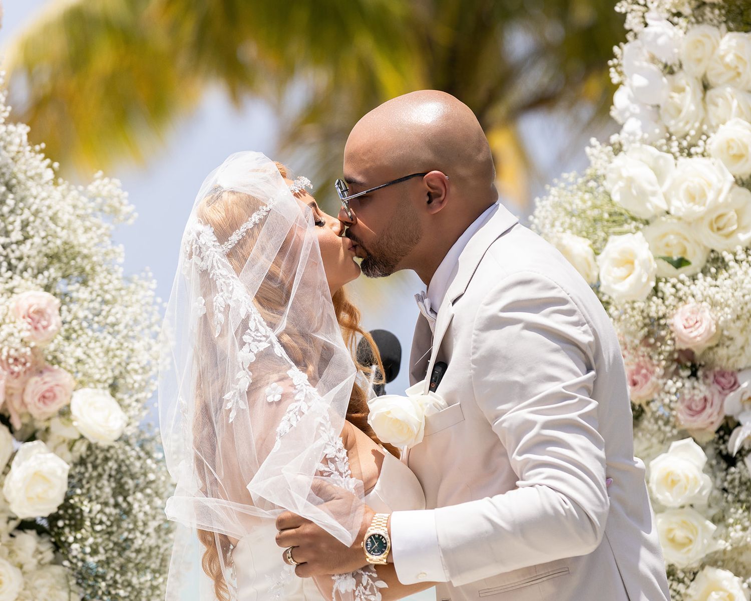 Romantic beach wedding ceremony with white floral arrangements and palm trees.