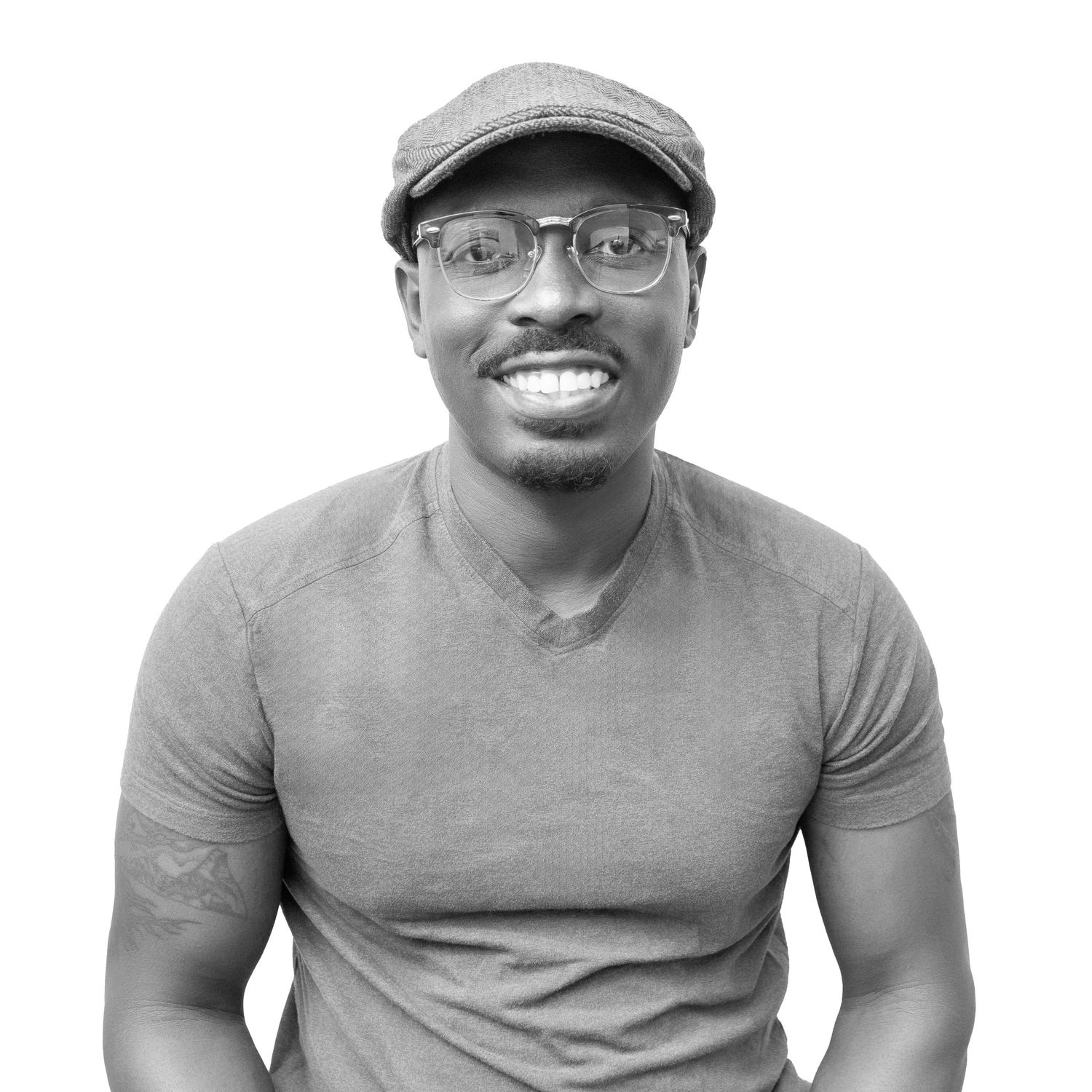 Professional headshot of someone wearing glasses, a cap and grey t-shirt against white background.