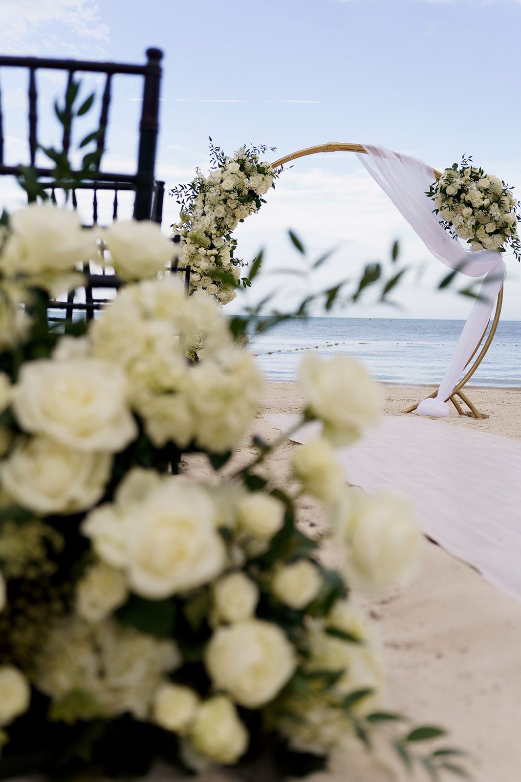 Elegant beach wedding setup with white rose arrangements and floral arch overlooking the ocean.