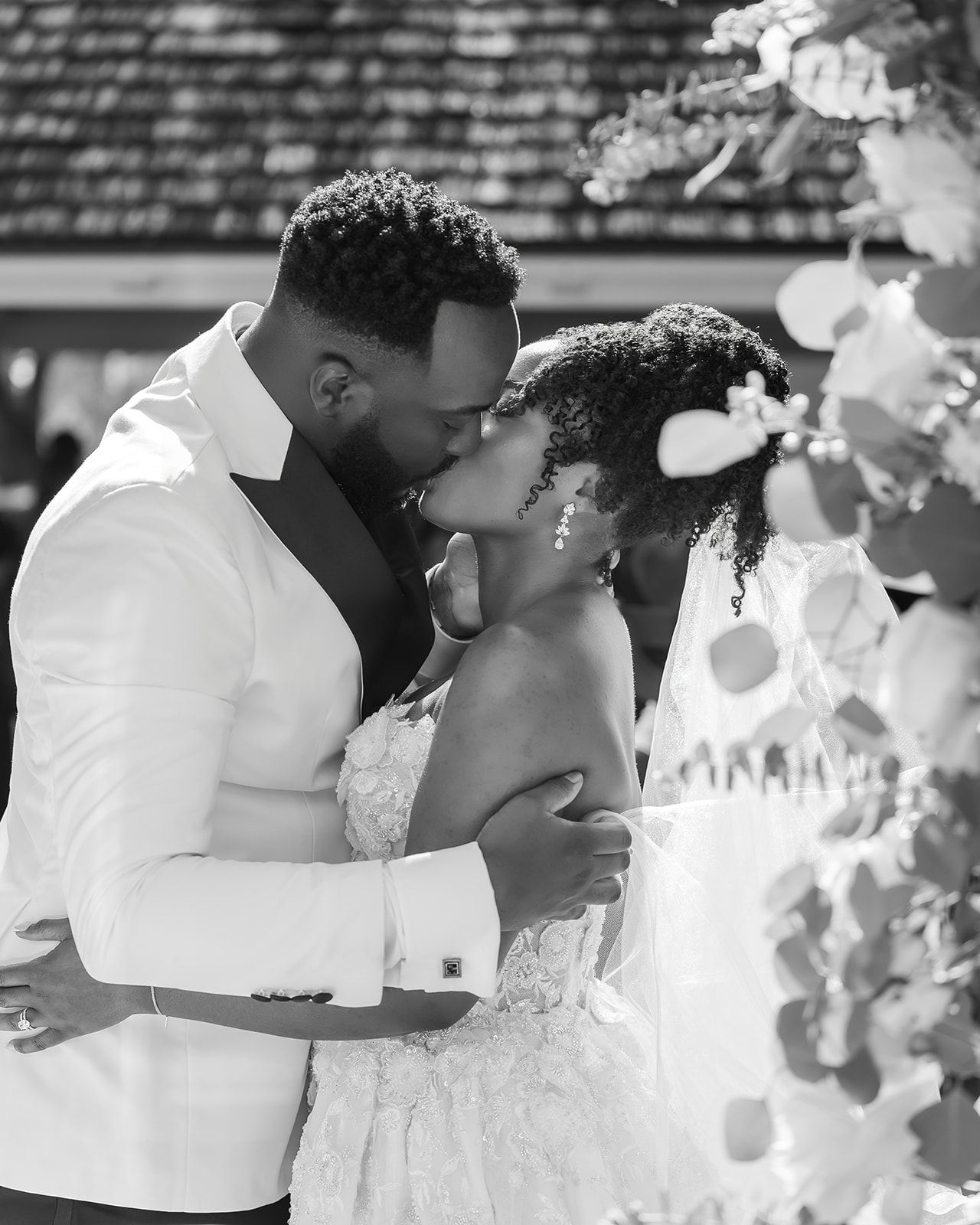 Black and white photo of newlyweds sharing their first kiss at outdoor wedding ceremony.