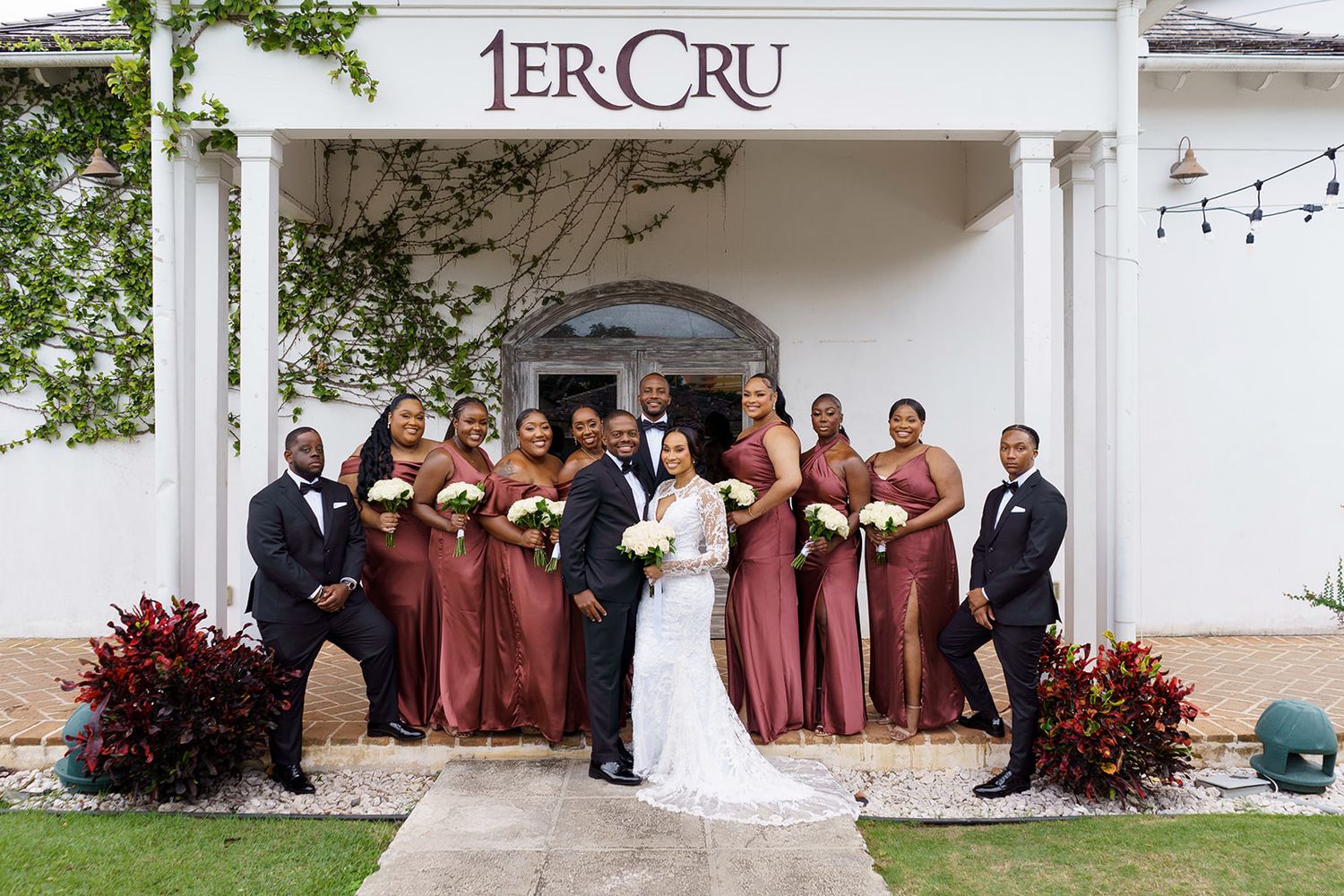 Wedding party posing outside 1er Cru venue, bridesmaids in dusty rose gowns with groomsmen in black suits.