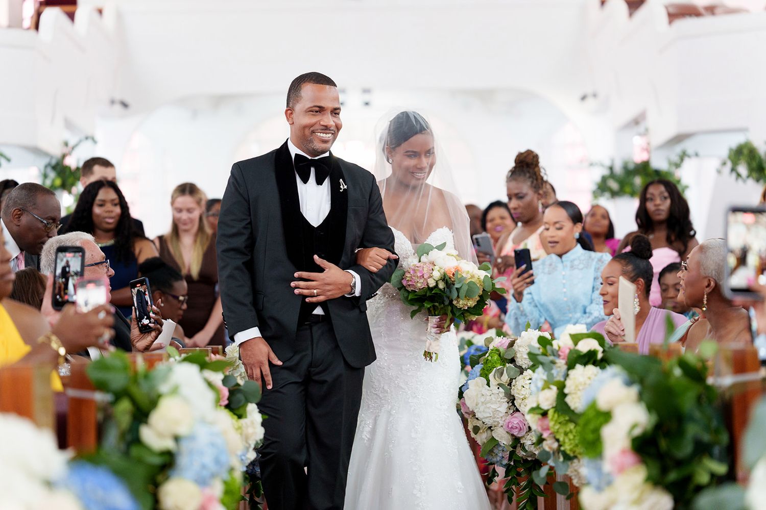 Bride and groom walking down the aisle at an elegant wedding ceremony with guests seated on both sides.