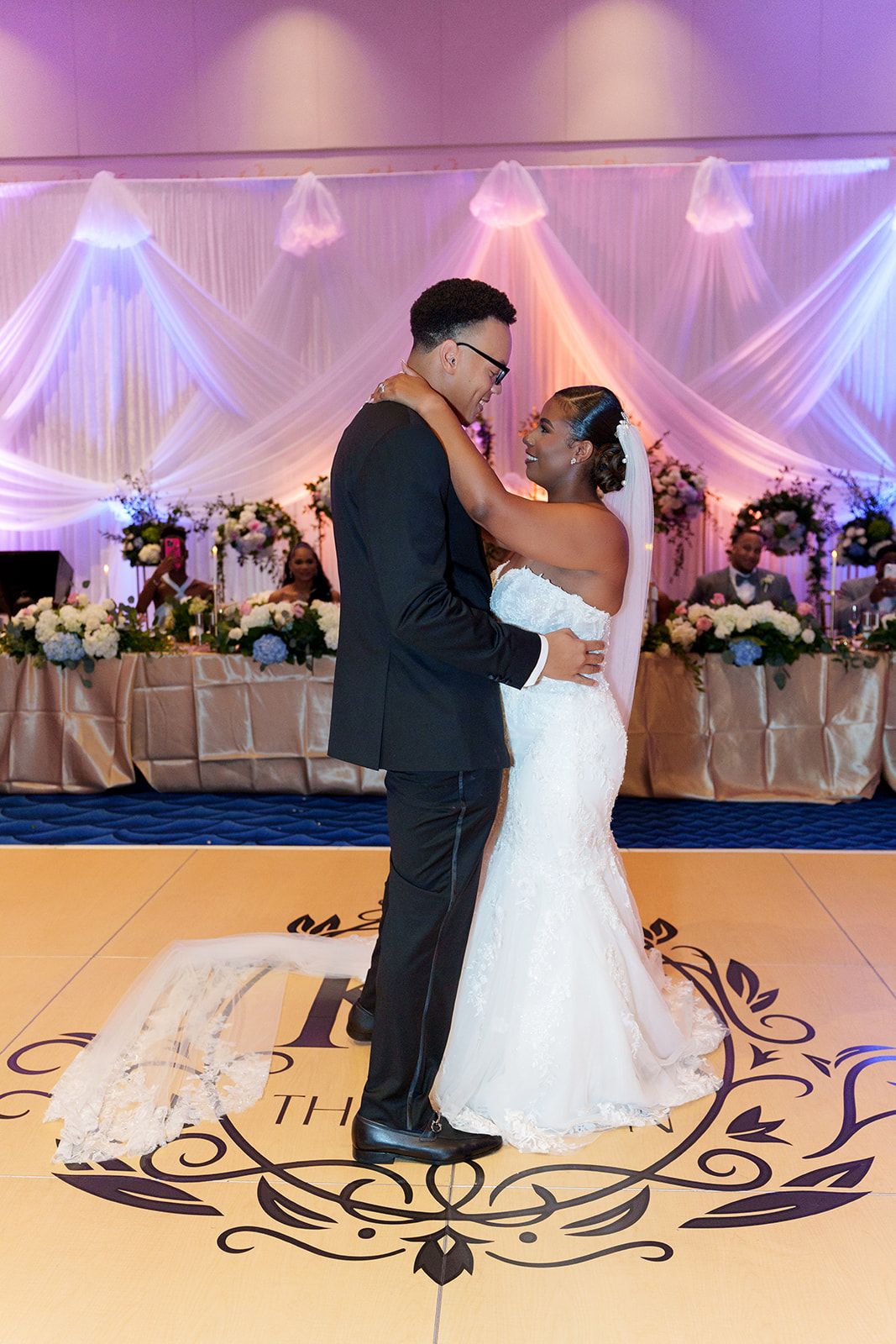 Bride and groom share their first dance on a monogrammed dance floor at their elegant wedding reception.
