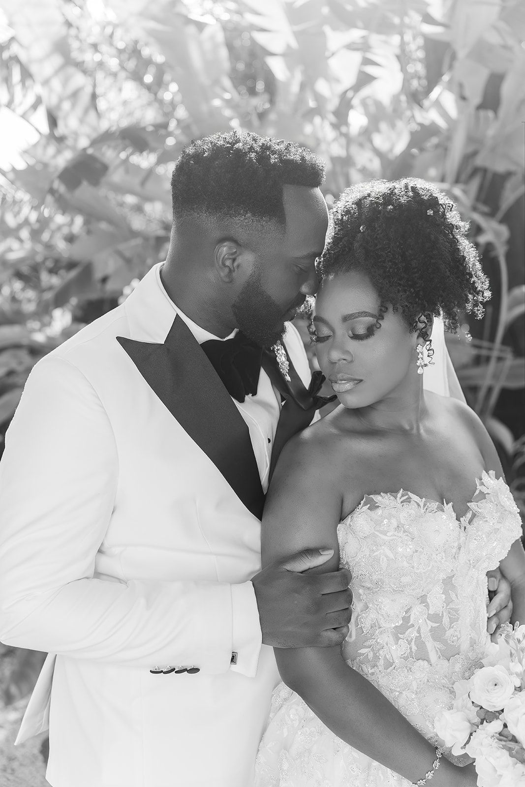 Black and white romantic portrait of bride and groom embracing closely in a lush garden setting.
