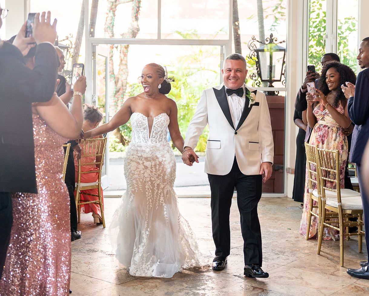 Newlyweds celebrate while walking down the aisle in a beautifully decorated venue with guests cheering.