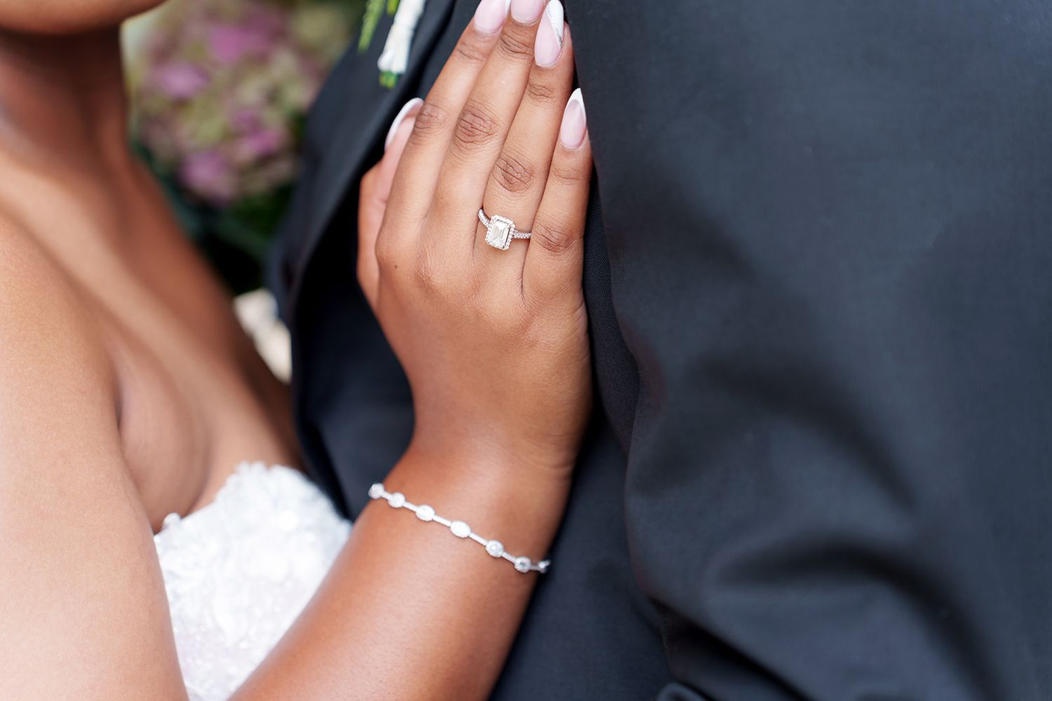 Close-up of bride's hand displaying elegant diamond engagement ring and delicate diamond bracelet on wedding day.