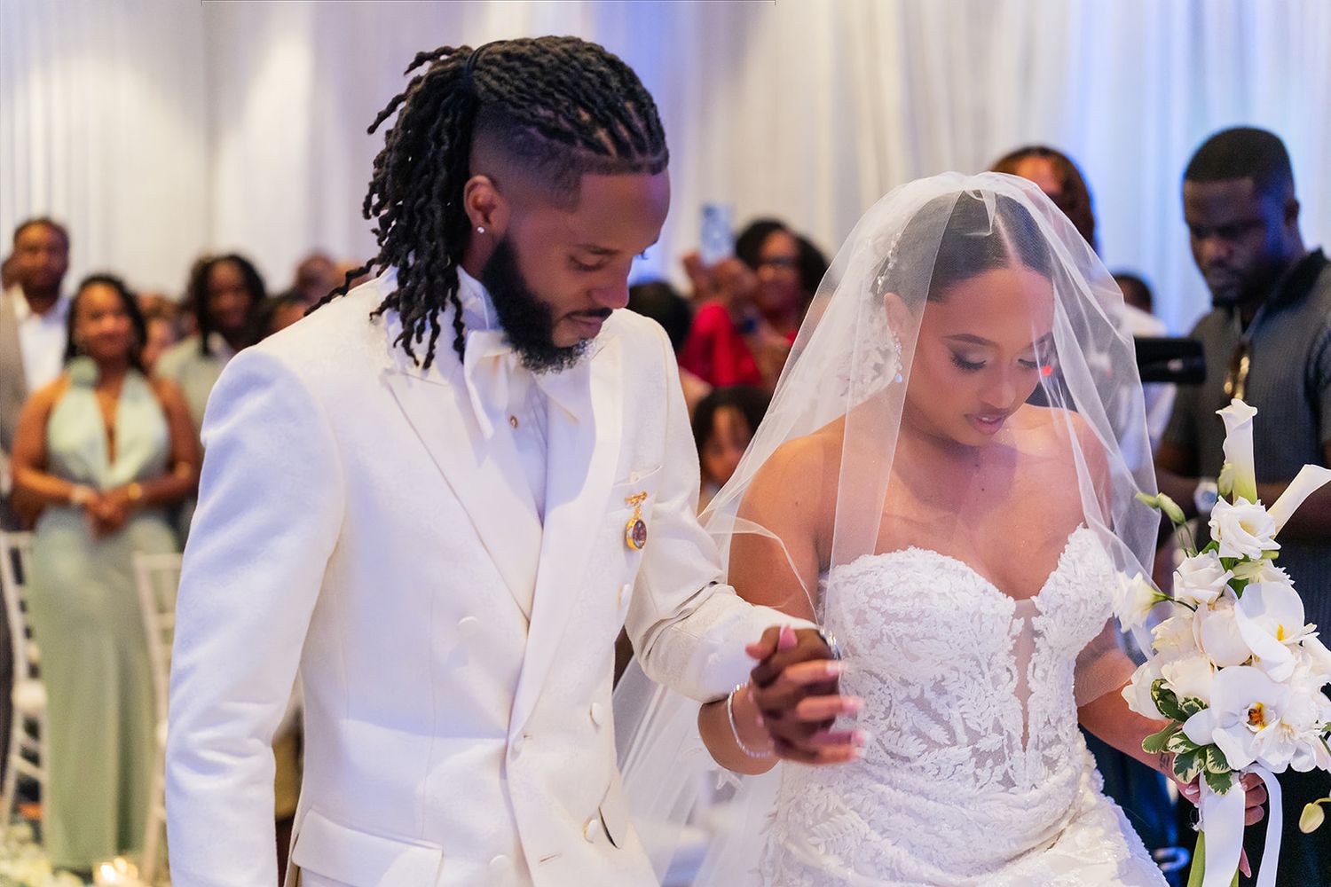 Bride and groom walking down the aisle at elegant wedding ceremony, groom in white suit, bride in lace gown with veil.
