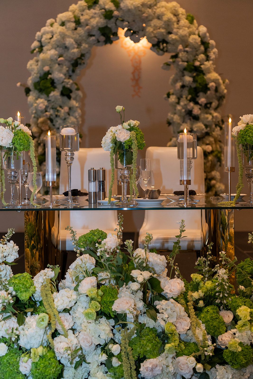 Elegant wedding sweetheart table with white and green floral arch, candlesticks, and lush flower arrangements.