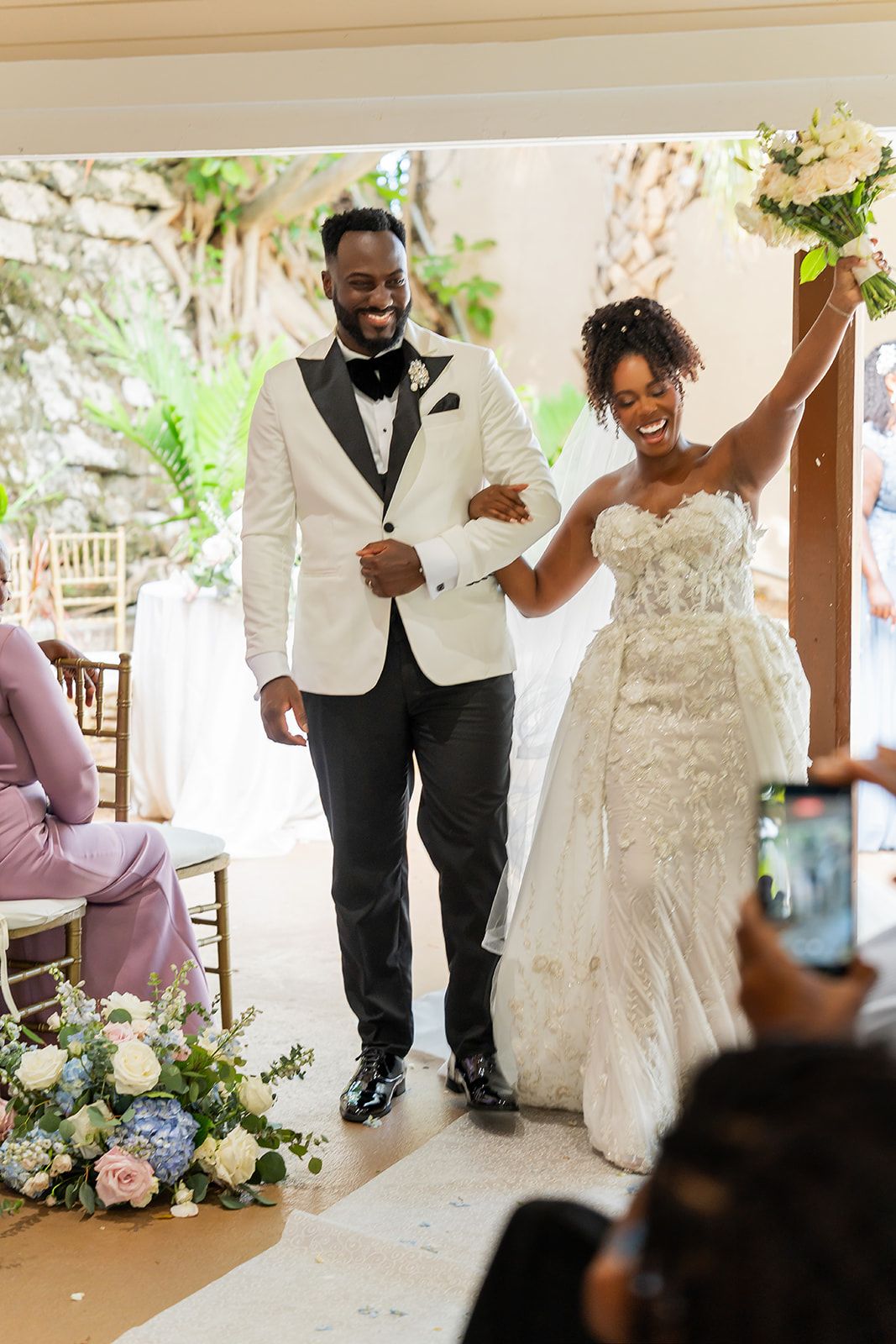 Joyful newlyweds celebrate as bride raises bouquet while exiting wedding ceremony.