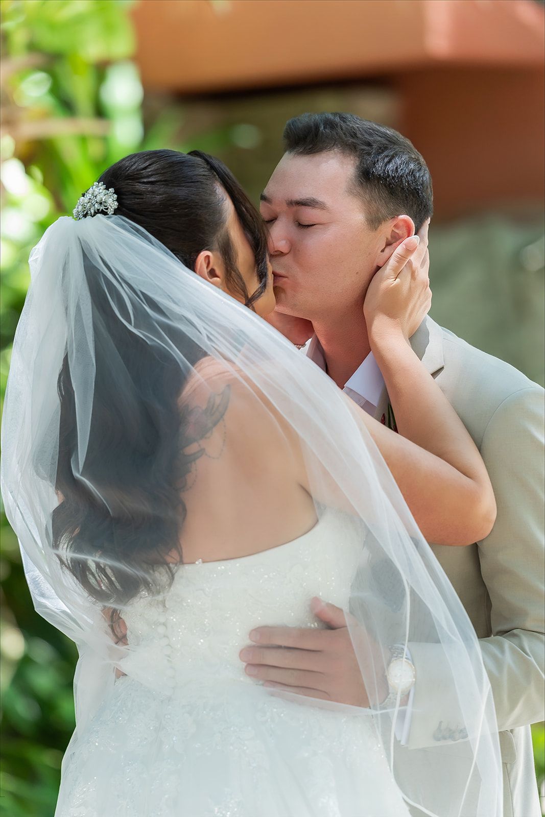 A bride and groom share a romantic first kiss at their outdoor wedding ceremony, with her white veil flowing gracefully.