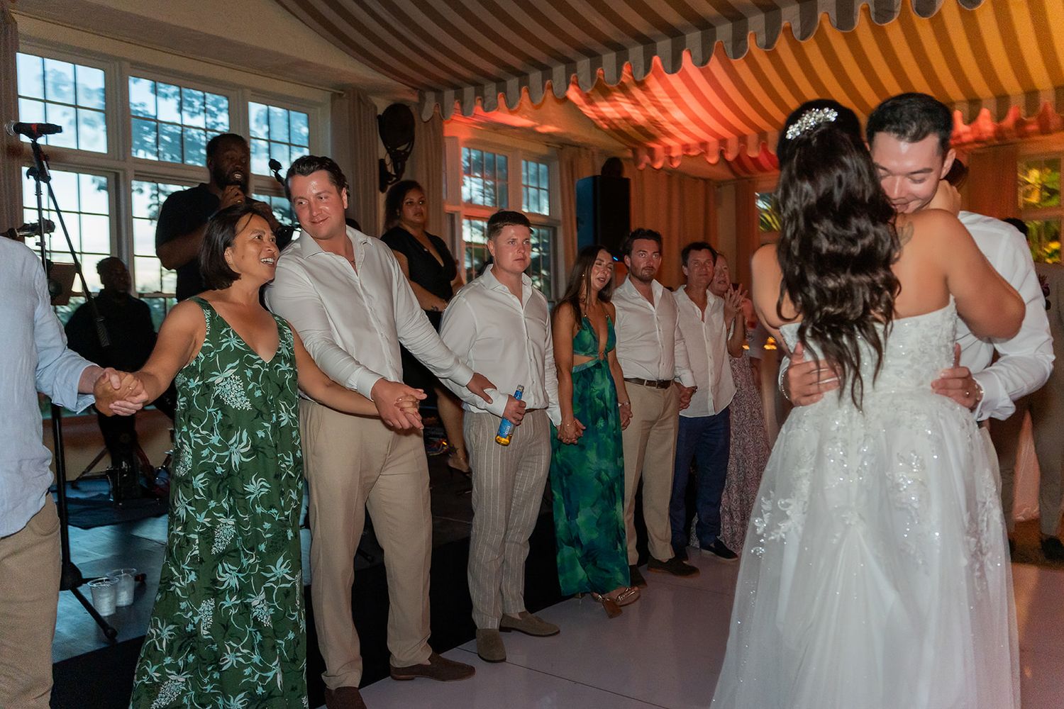 Bride and groom share first dance surrounded by wedding party guests at elegant indoor reception venue.