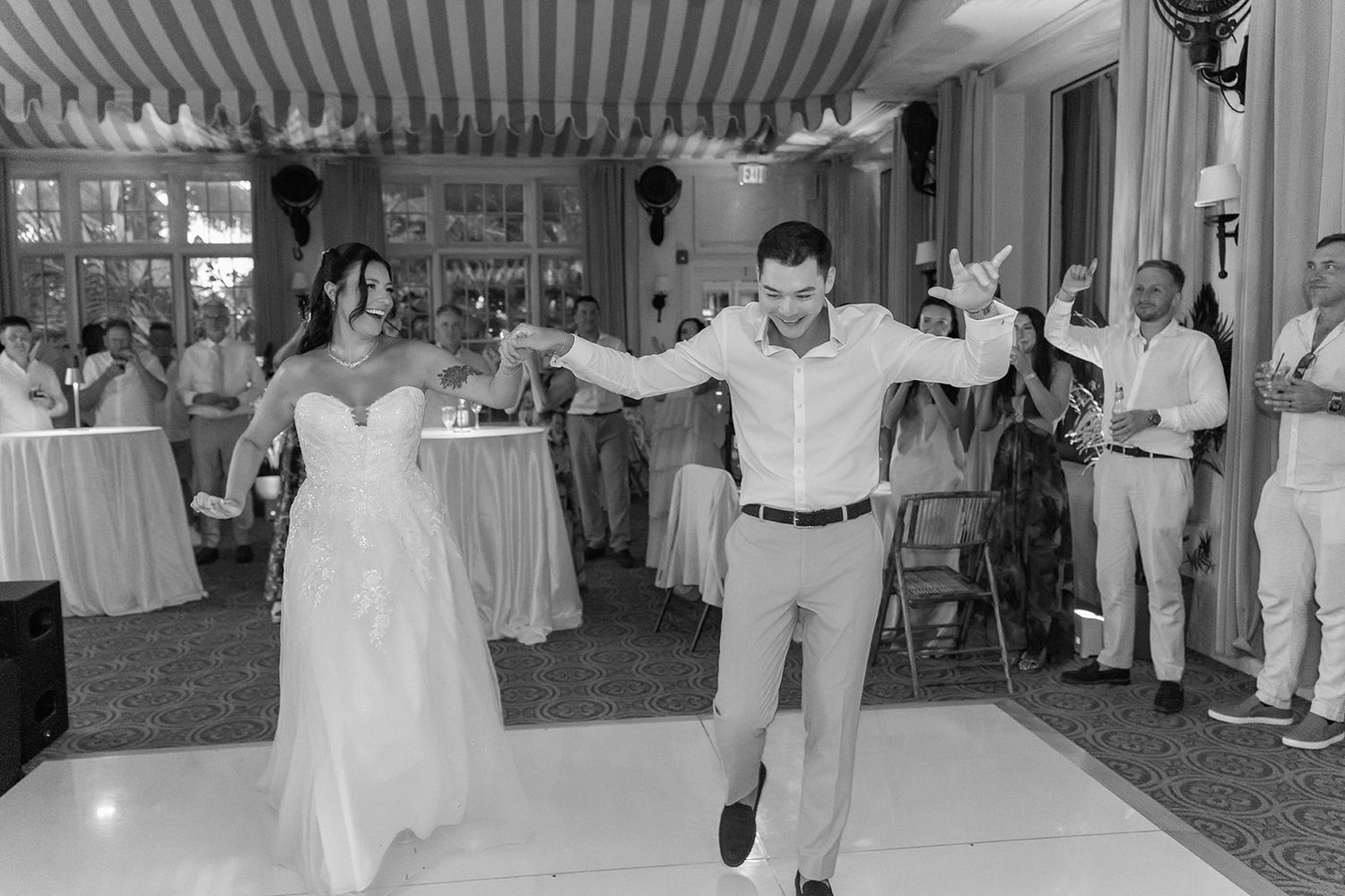 Bride and groom joyfully dancing at wedding reception in elegant venue with guests celebrating in background.