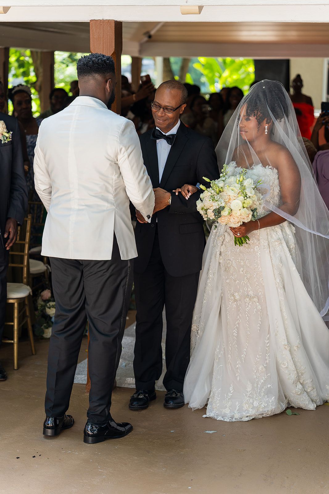 Father of the bride presents daughter to groom during outdoor wedding ceremony under pavilion.