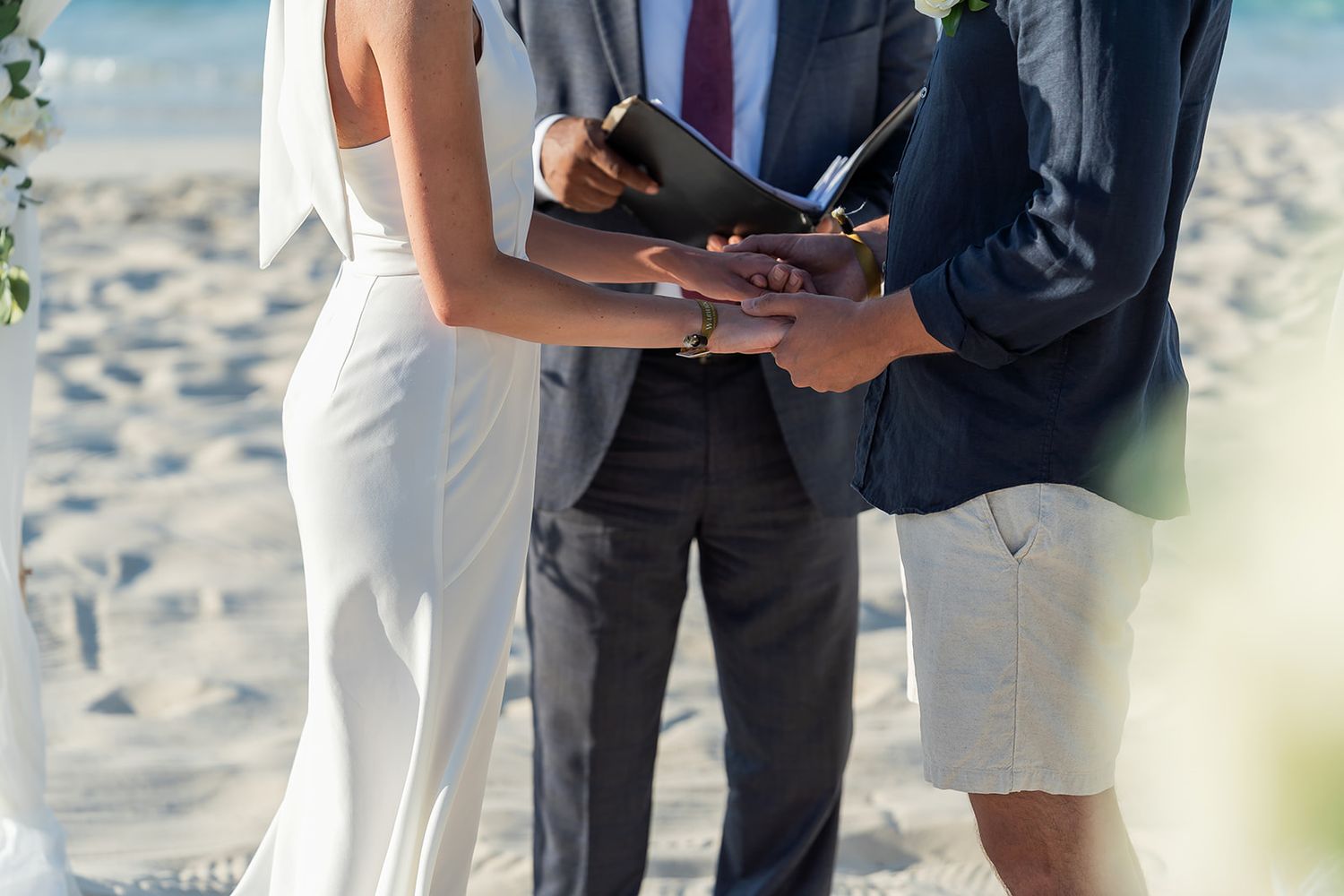 Couple exchanging rings during a romantic beach wedding ceremony with an officiant holding a book.