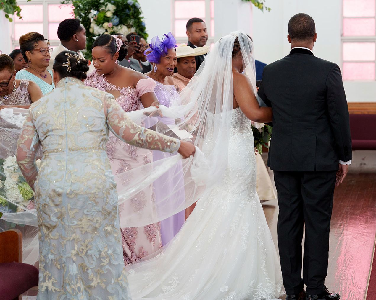 Bride in white gown and veil assisted by guests at a church wedding ceremony.