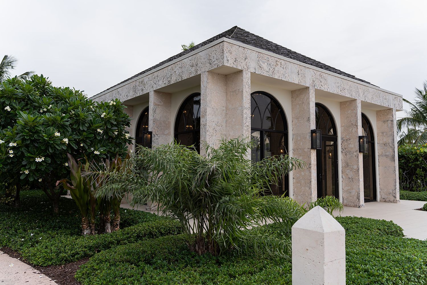 Elegant limestone pavilion with arched windows surrounded by lush tropical landscaping in a Florida estate.