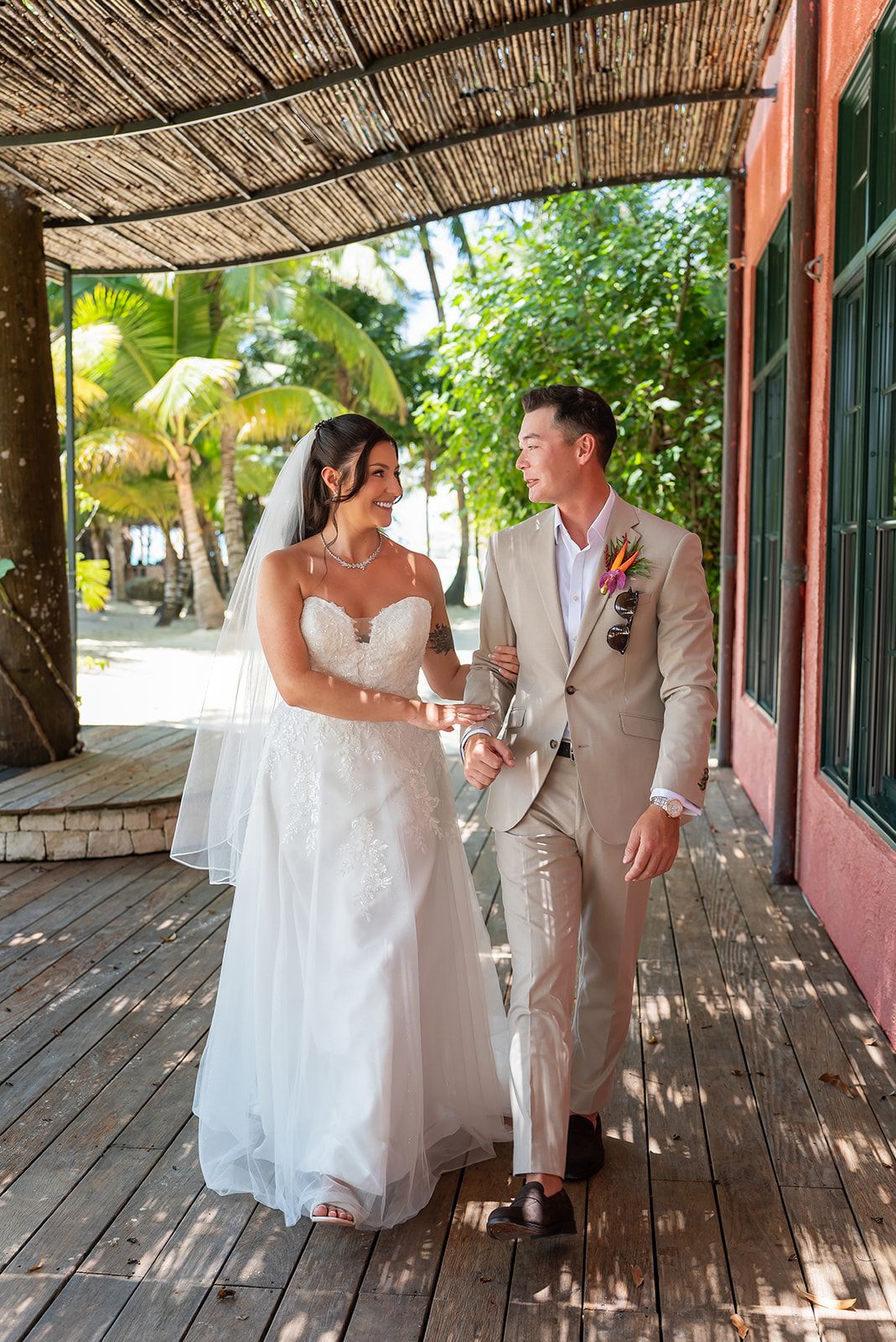 Bride and groom walking together on a wooden deck surrounded by tropical palms at a destination wedding.