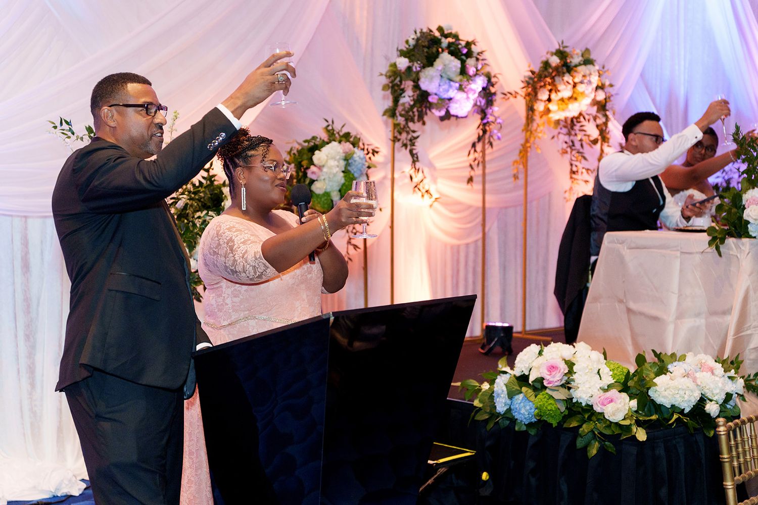 Bride and groom raising glasses in a toast at their elegant wedding reception with floral decorations.