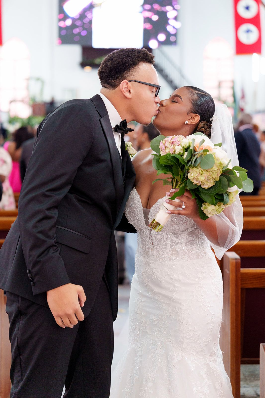 Bride and groom share a first kiss at the altar in a church wedding ceremony, bride holding white floral bouquet.
