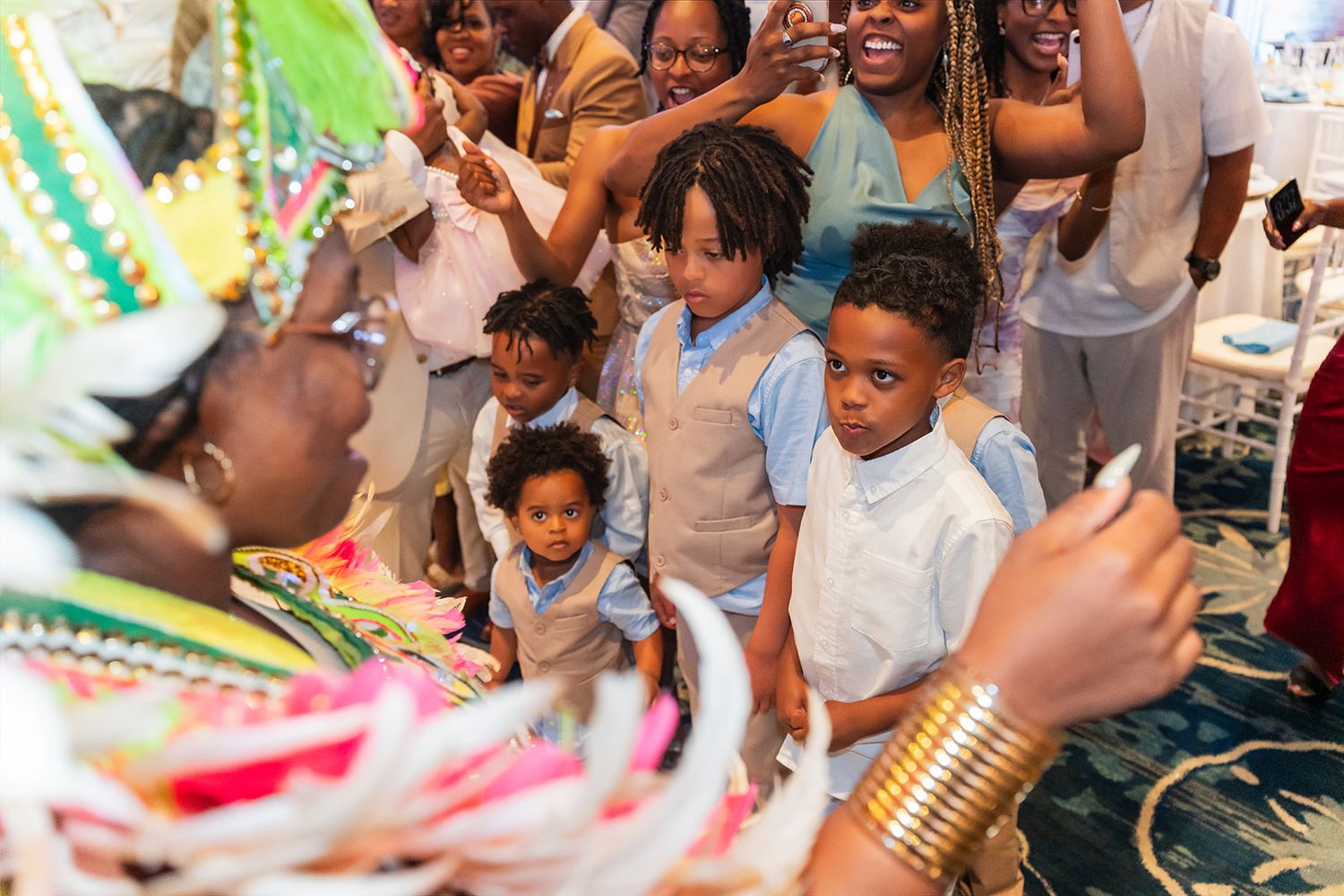 Children watch a colorful Caribbean performer in traditional costume at a festive indoor cultural celebration.
