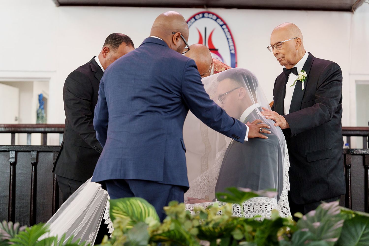 Men in formal attire adjusting a brides veil before a church wedding ceremony.