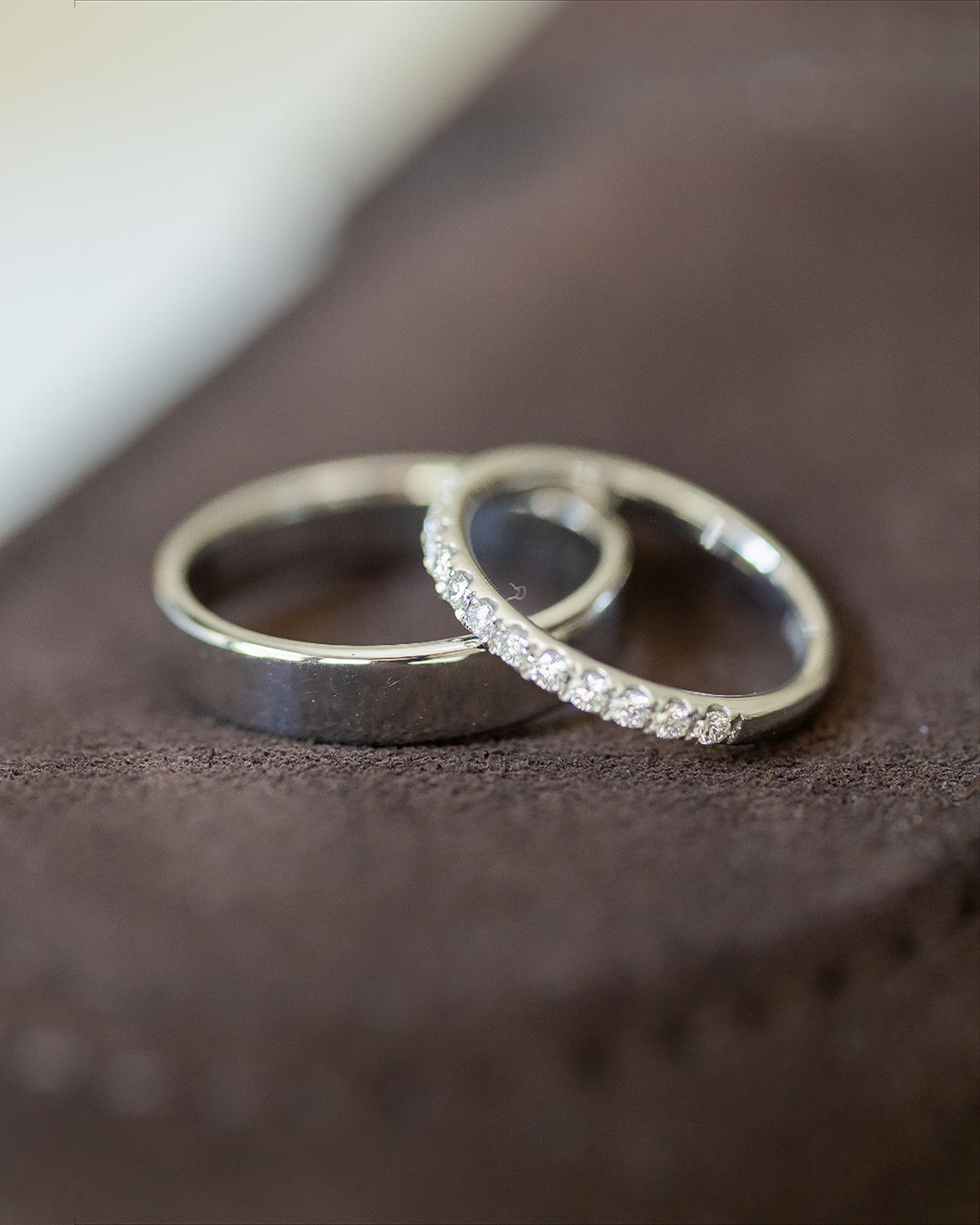 Two silver wedding bands, one plain and one diamond-encrusted eternity ring, resting on a dark brown surface.