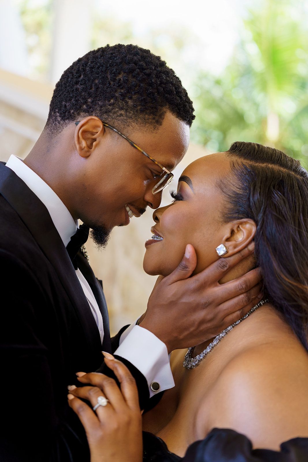 A couple in formal attire shares a romantic moment, the man in a tuxedo gently holding the woman's face as they lean in for a kiss.